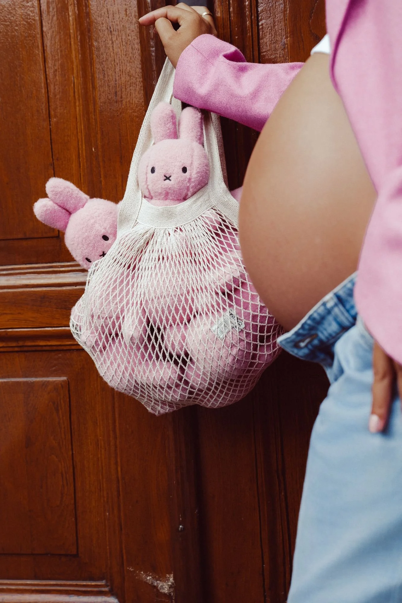 Person in pink shirt hanging a white mesh bag filled with pink stuffed bunny toys on a wooden door