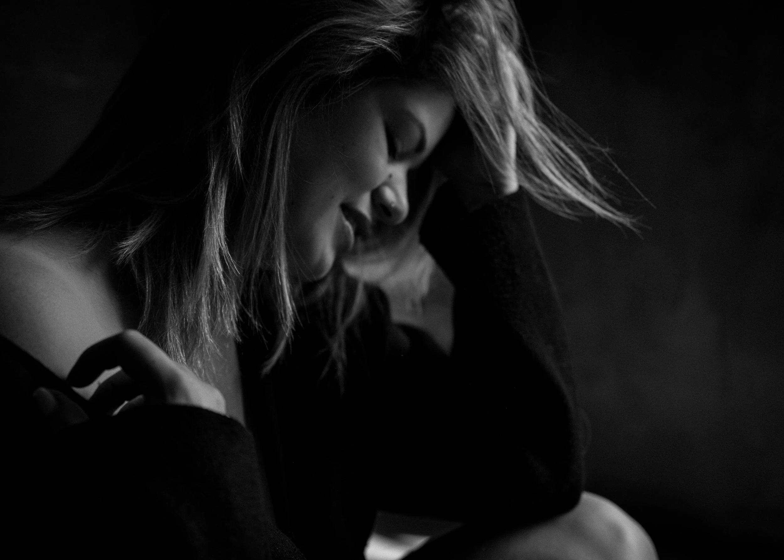 Zwart-wit portret van een vrouw met lang golvend haar, rustend met haar voorhoofd op haar hand — een zacht, reflectief moment.