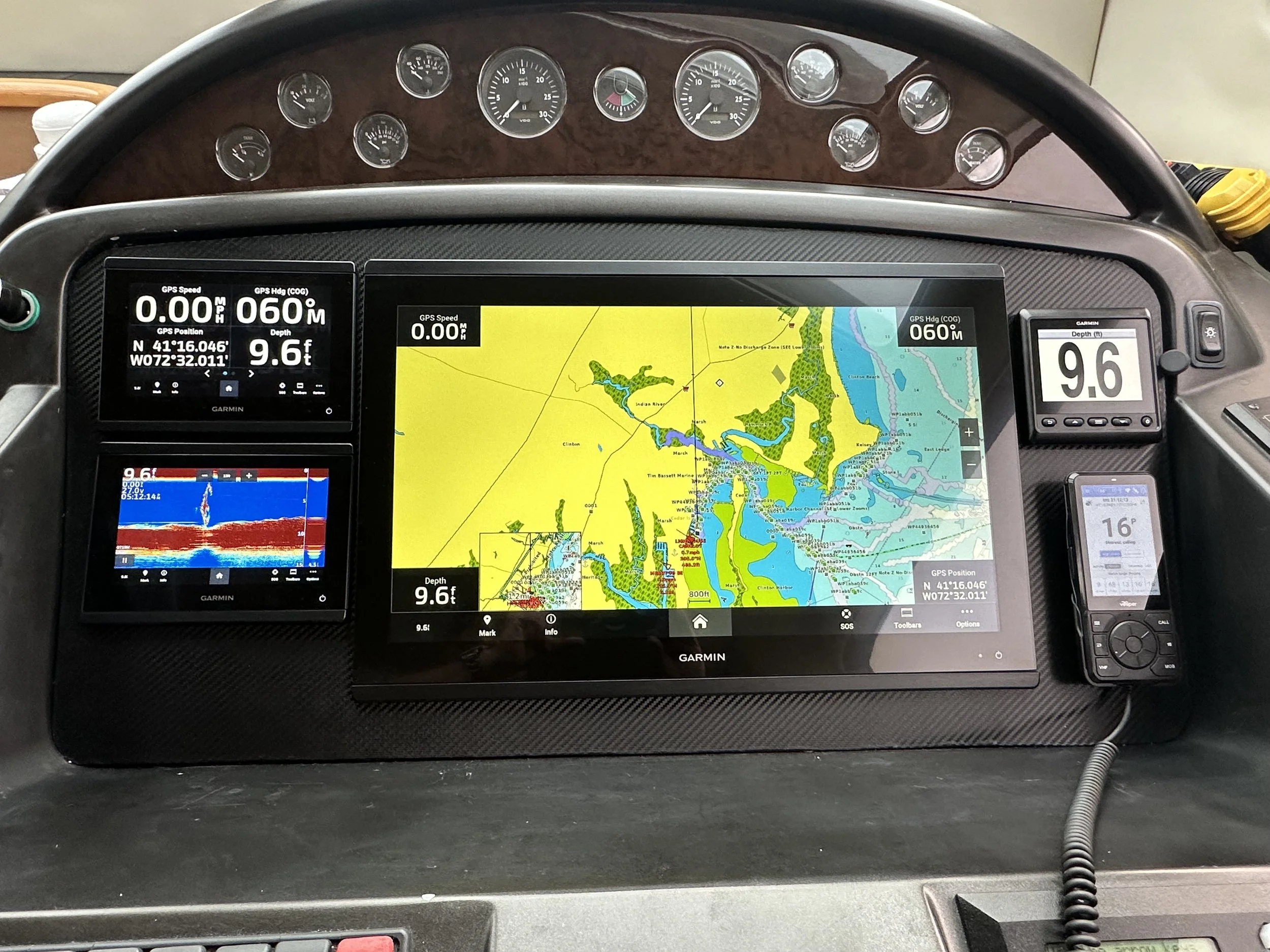 Nighttime view of the top of a yacht with radar and communication equipment, illuminated by blue lights, with a dark sky and docked boats in the background.