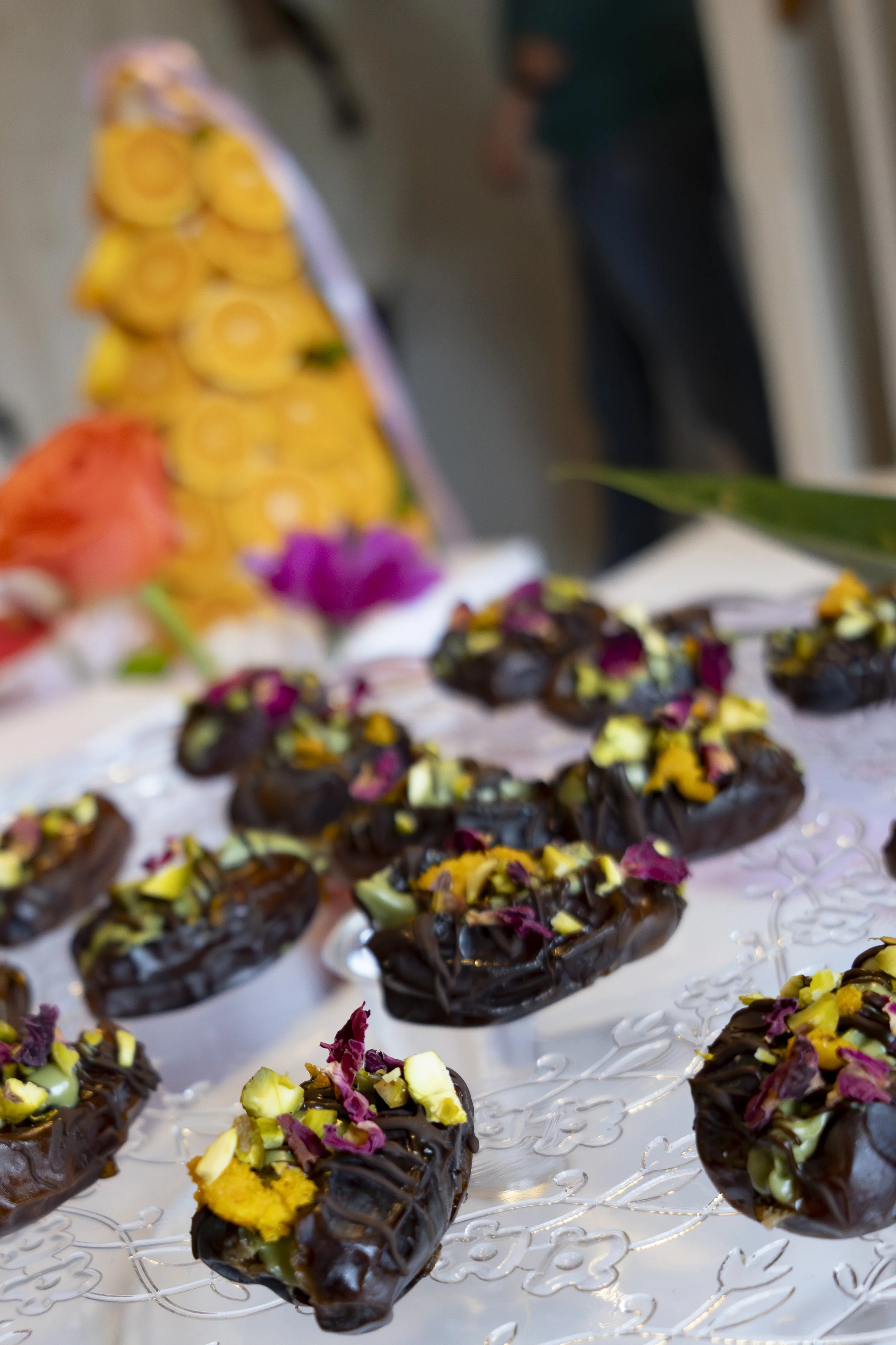 Chocolate-dipped pastries topped with chopped pistachios and rose petals on a glass tray.