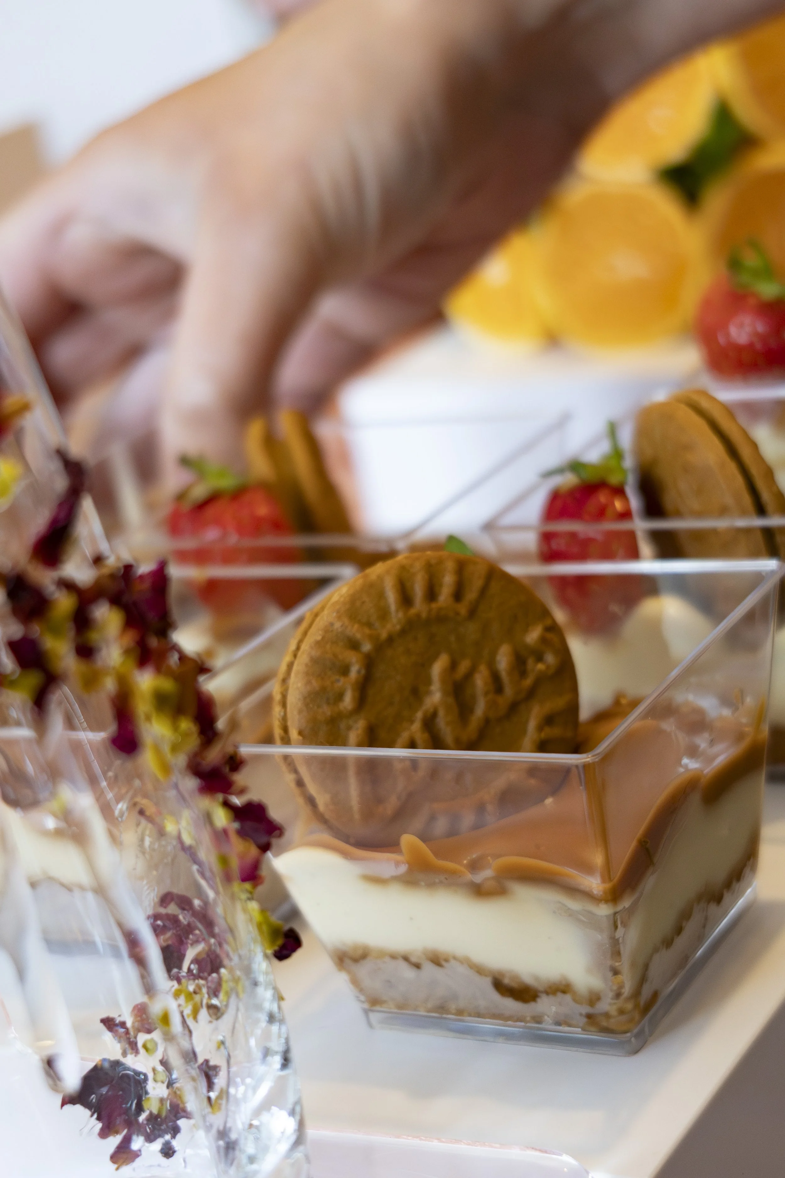 Close-up of a layered dessert in a glass cup with cookies, strawberries, and caramel sauce, topped with whipped cream and garnishes.