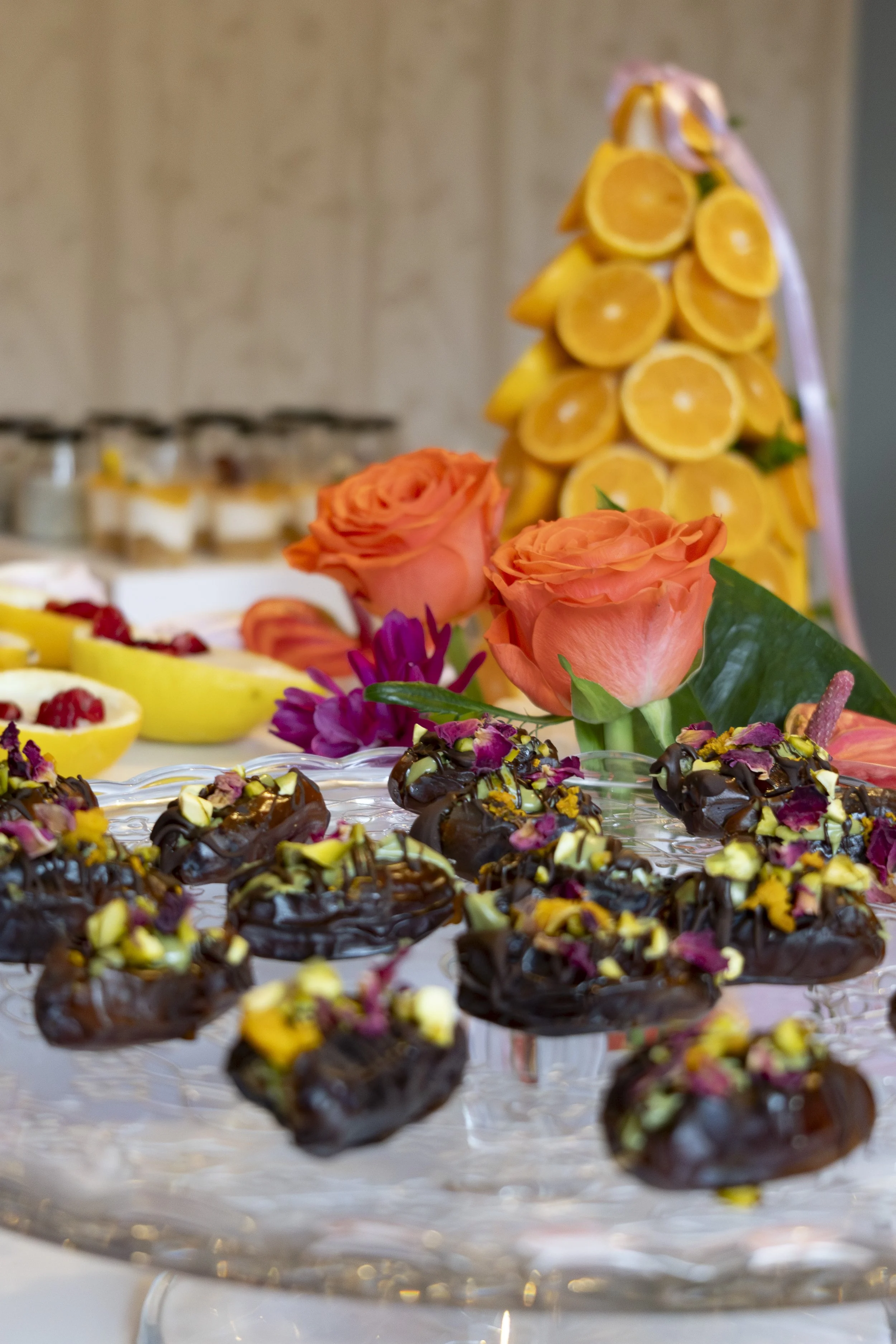 Chocolate dessert bites topped with chopped nuts and pink petals on a clear glass tray