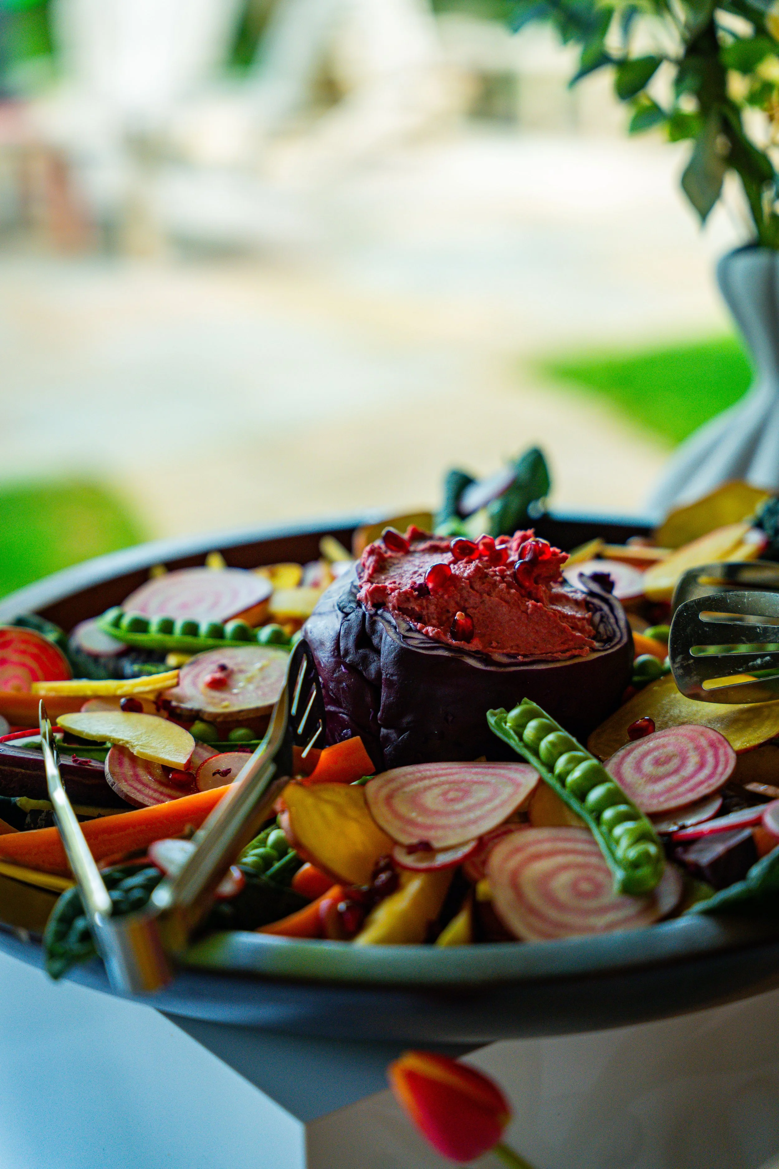 Close-up of a colorful vegetable platter with sliced beets, carrots, radishes, and snap peas, garnished with pomegranate seeds, on a light blue tray.