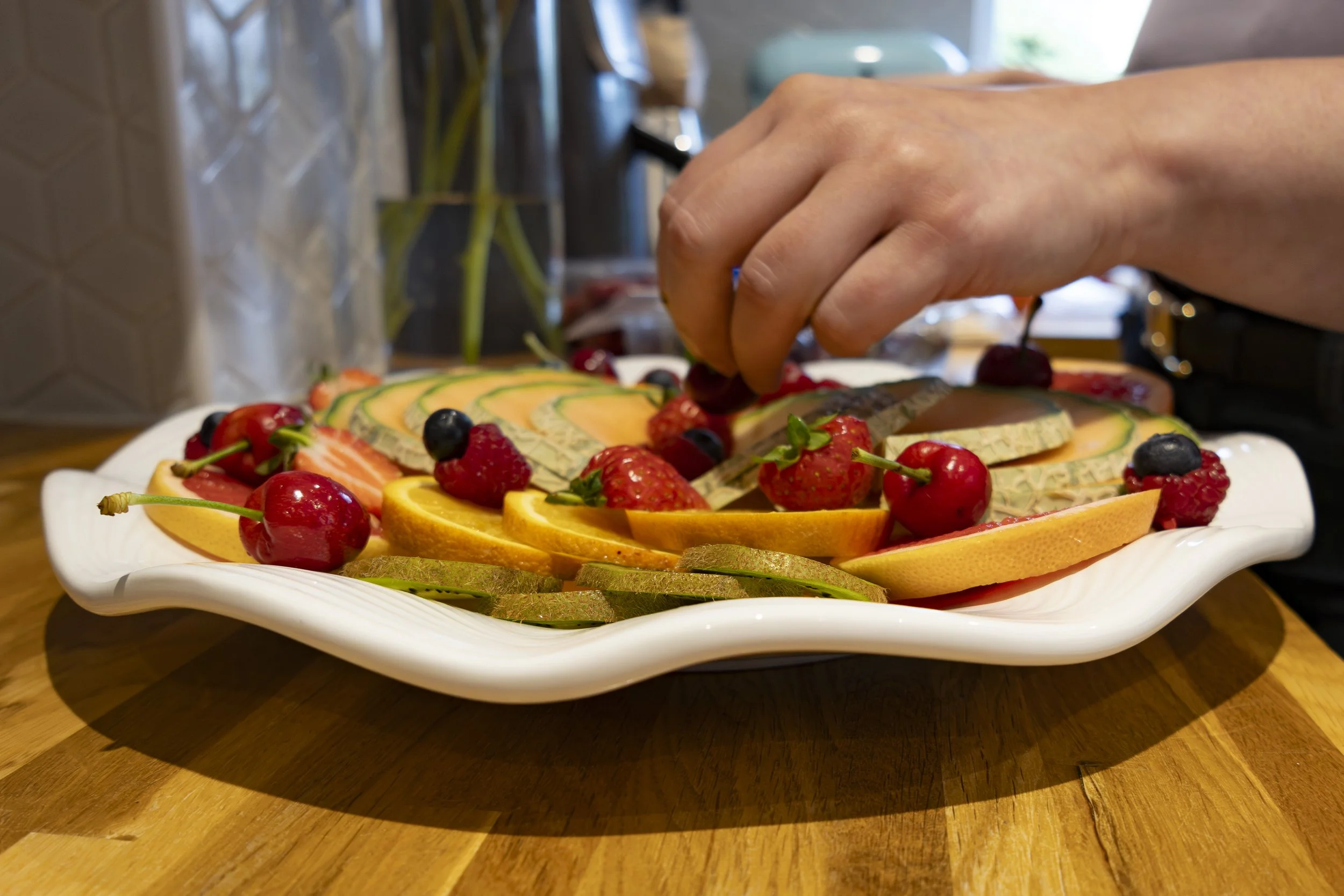 A person garnishing a plate of sliced fruits with berries on a wooden table.