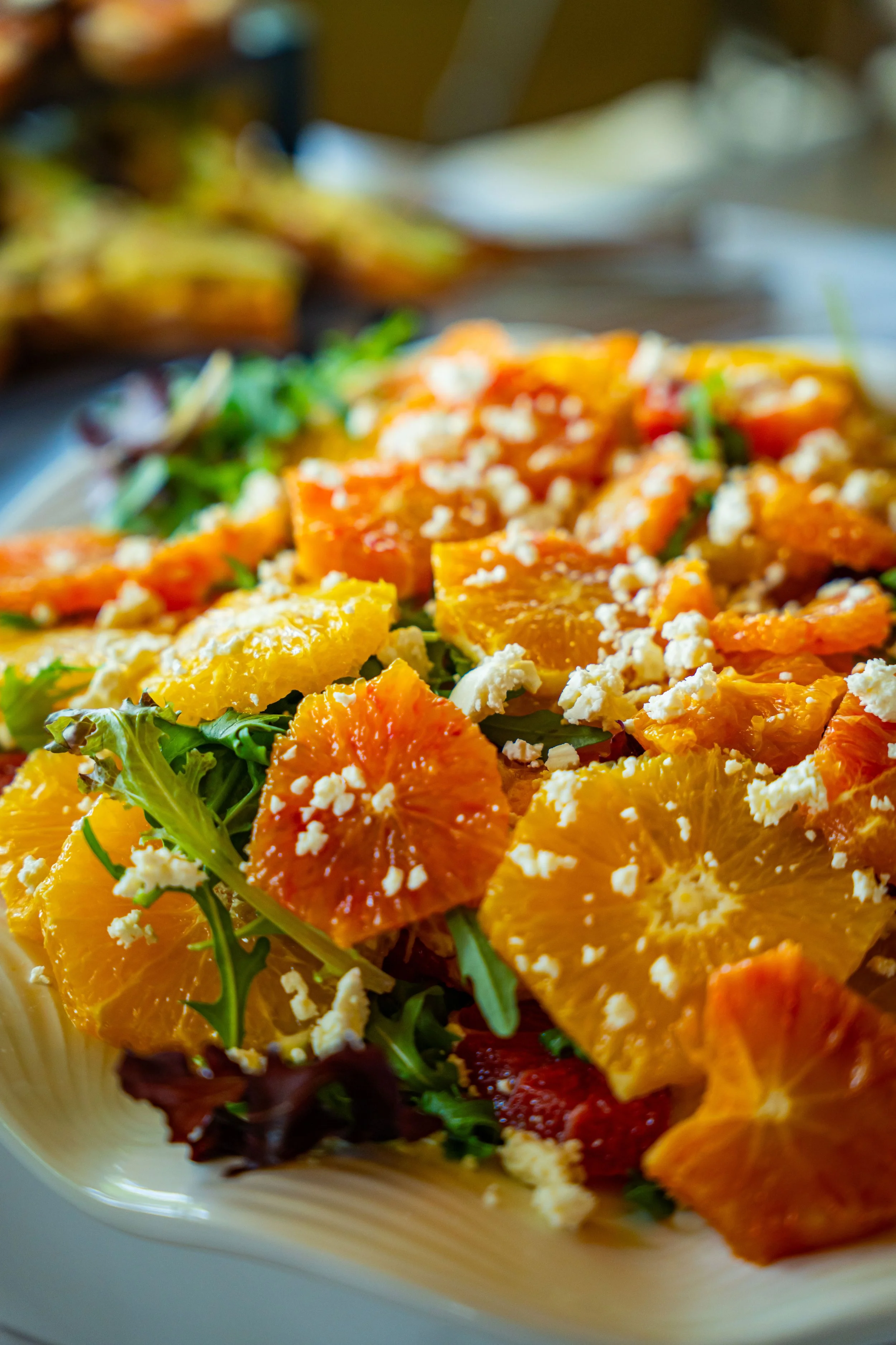 A close-up of a colorful salad with orange slices, crumbled cheese, and mixed greens in a white bowl.