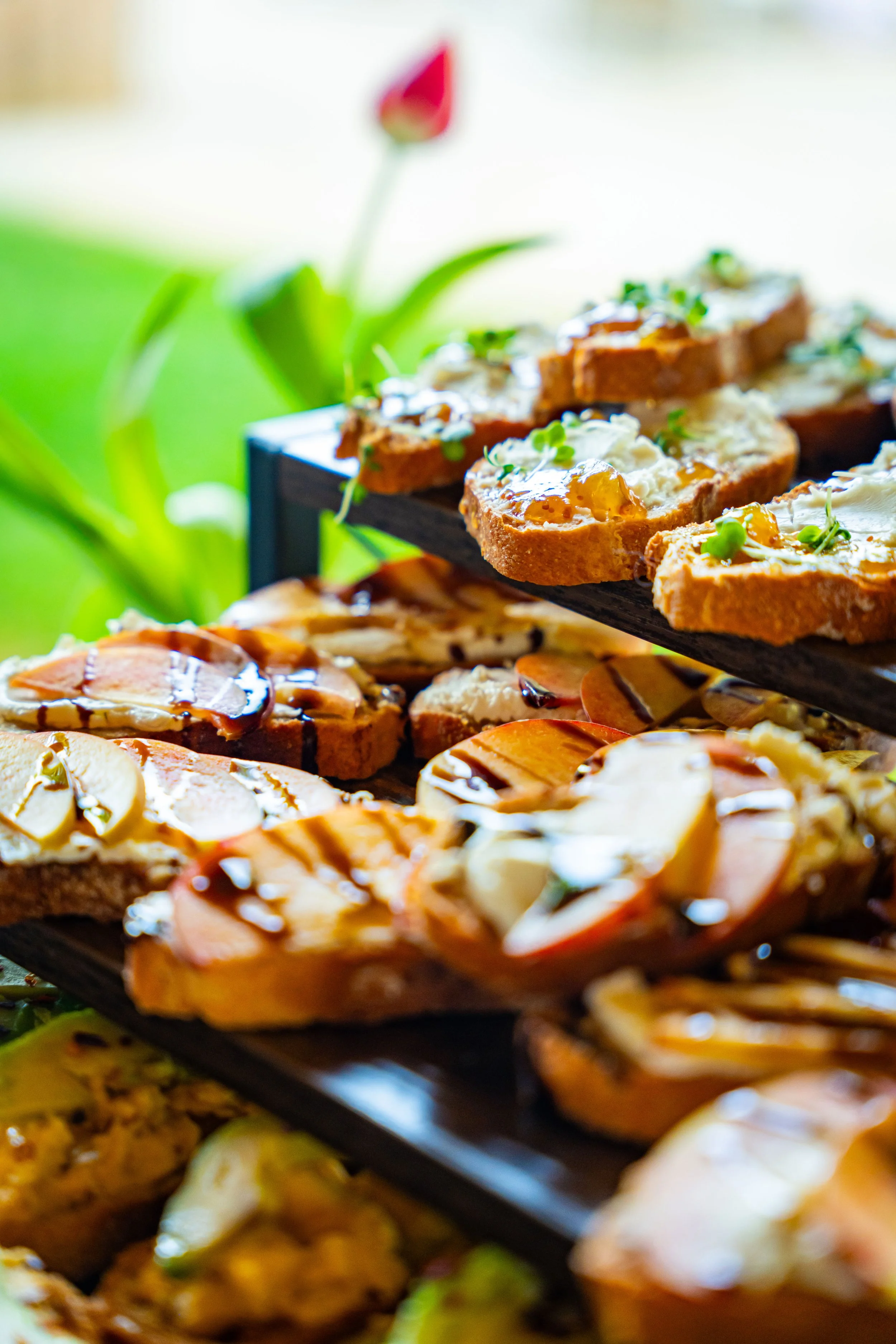 Close-up of various open-faced sandwiches with toppings like cheese, greens, and sauces on a multi-tiered serving tray.