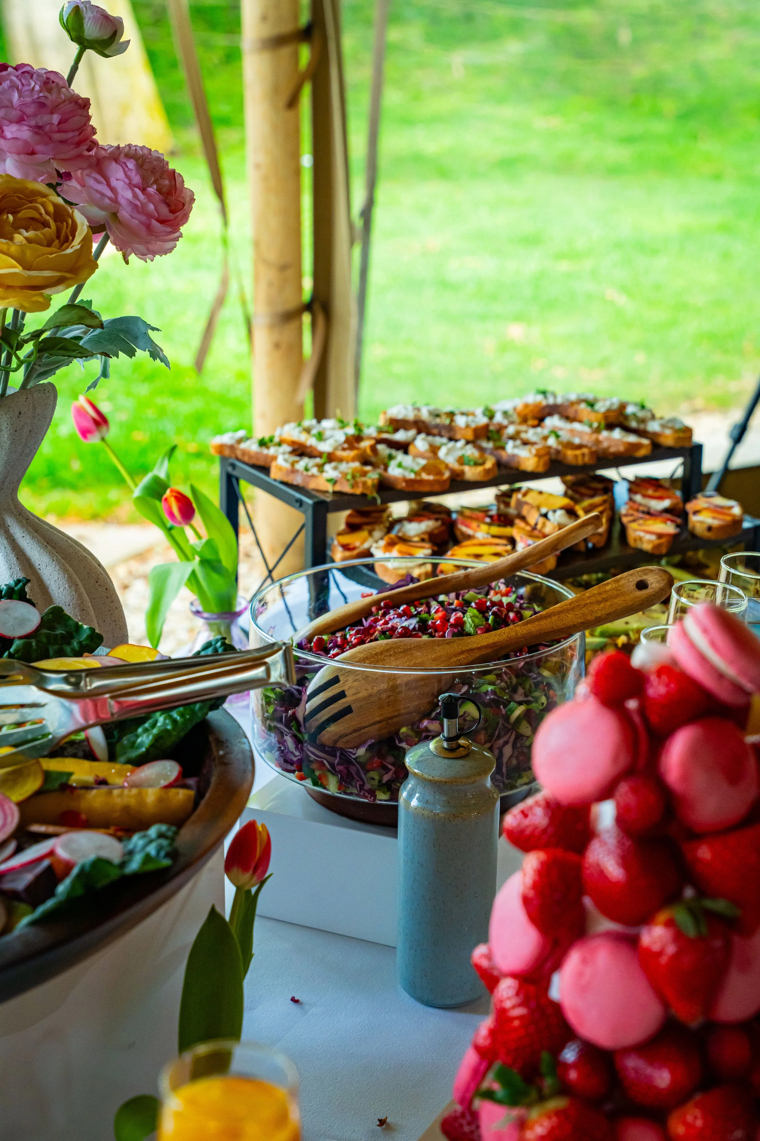 A buffet table with various colorful fruits, salads, and appetizers at an outdoor event with a green grassy background.