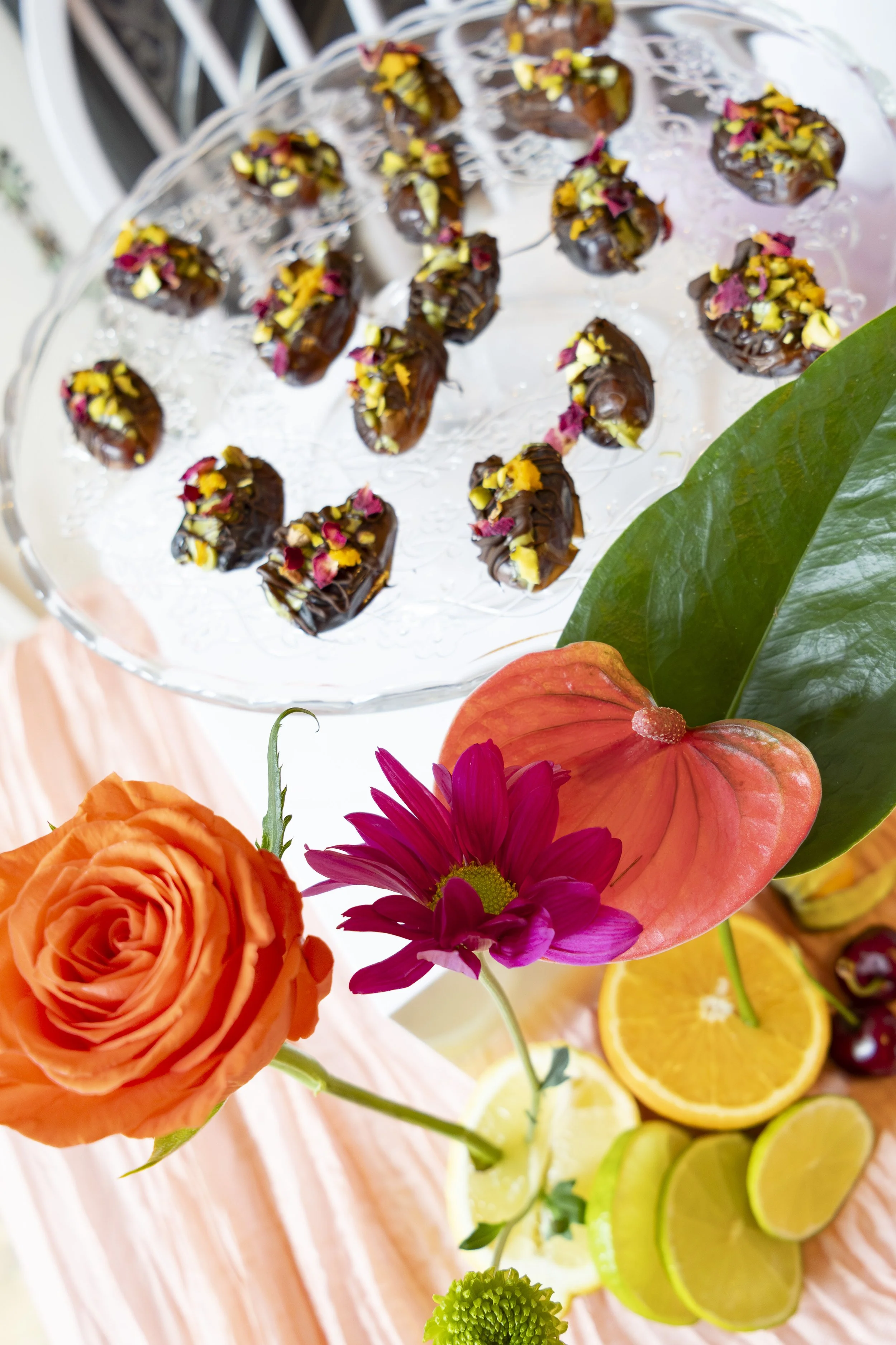 Colorful floral arrangement with orange roses, pink daisies, purple and yellow flowers, and slices of lemon, lime, and orange on a table.