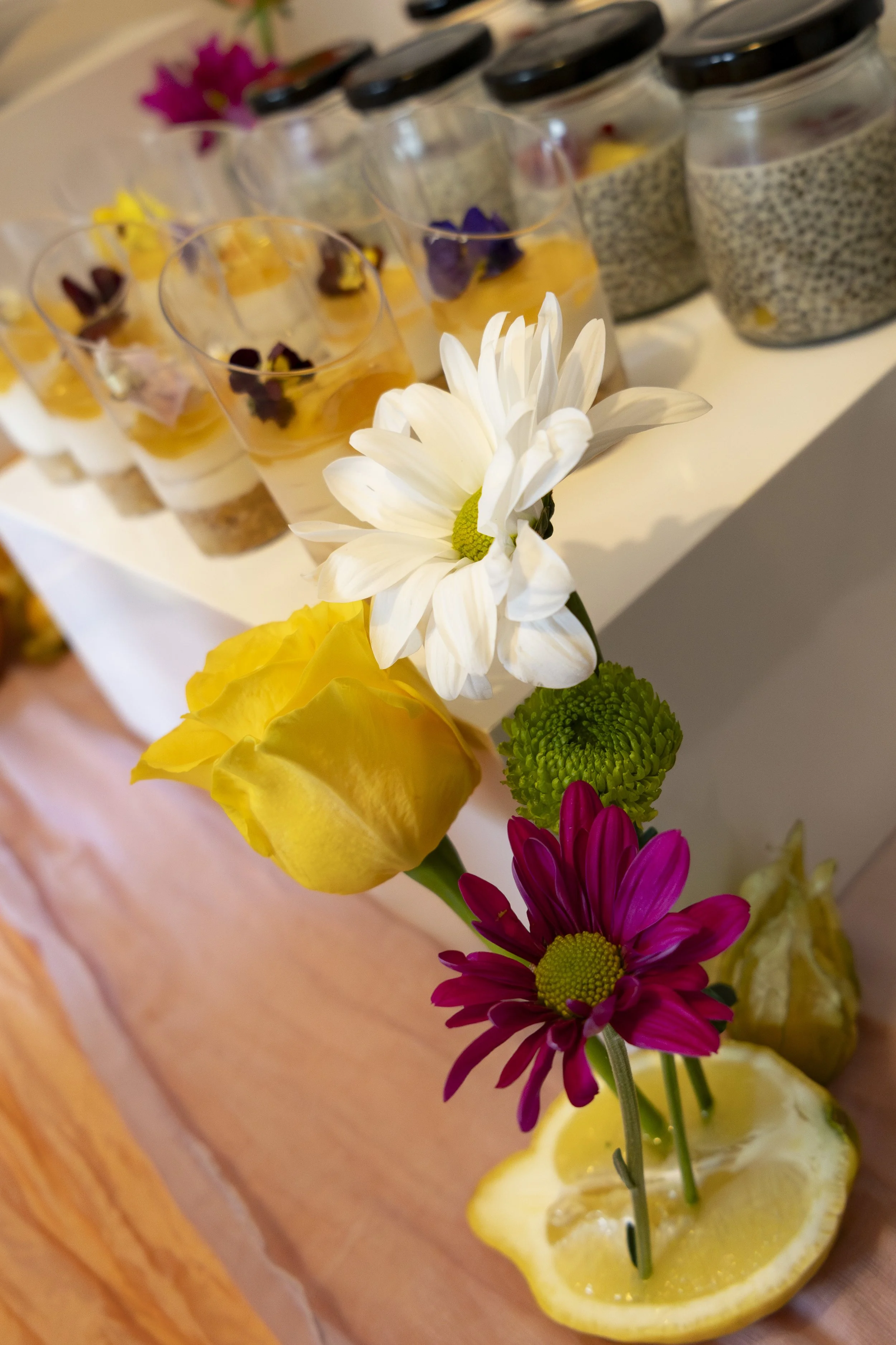 Assorted flowers and beverages on a wooden table, with jars and slices of lemon.