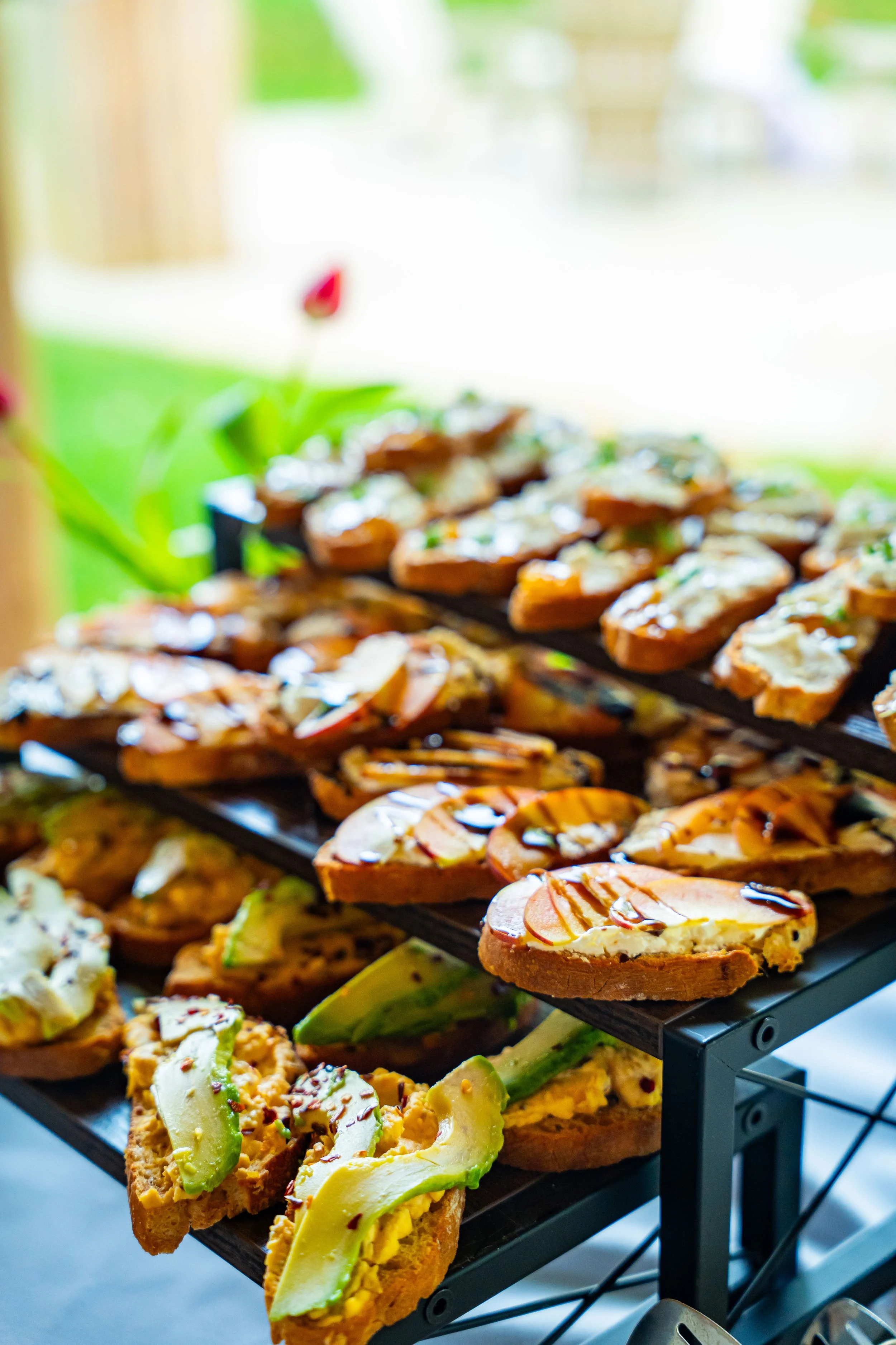 Assorted open-faced sandwiches with various toppings arranged on a multi-tiered serving tray near a window.