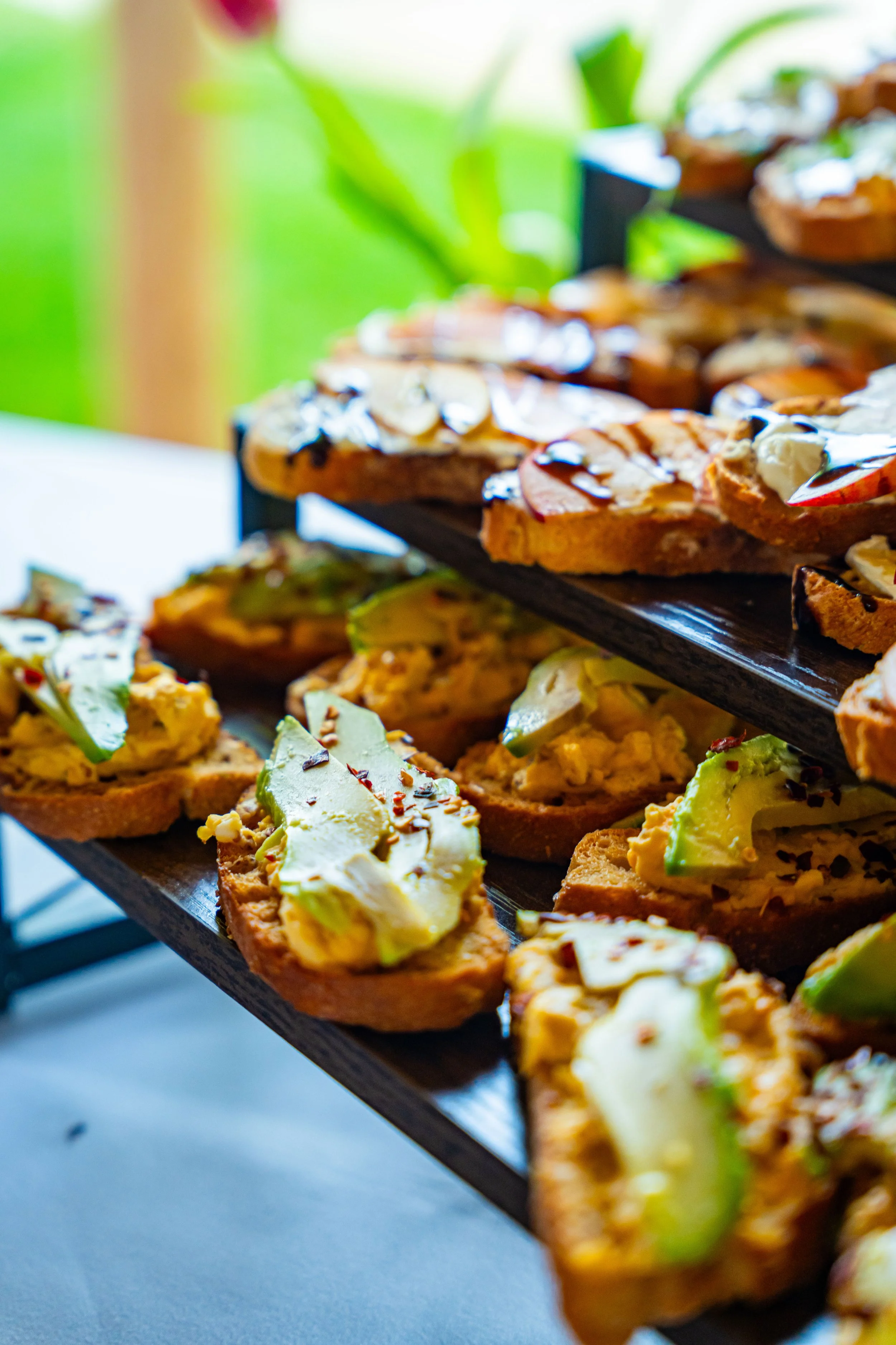 Close-up of assorted bruschetta appetizers with toppings like cheese, avocado, and herbs on a wooden serving tray.