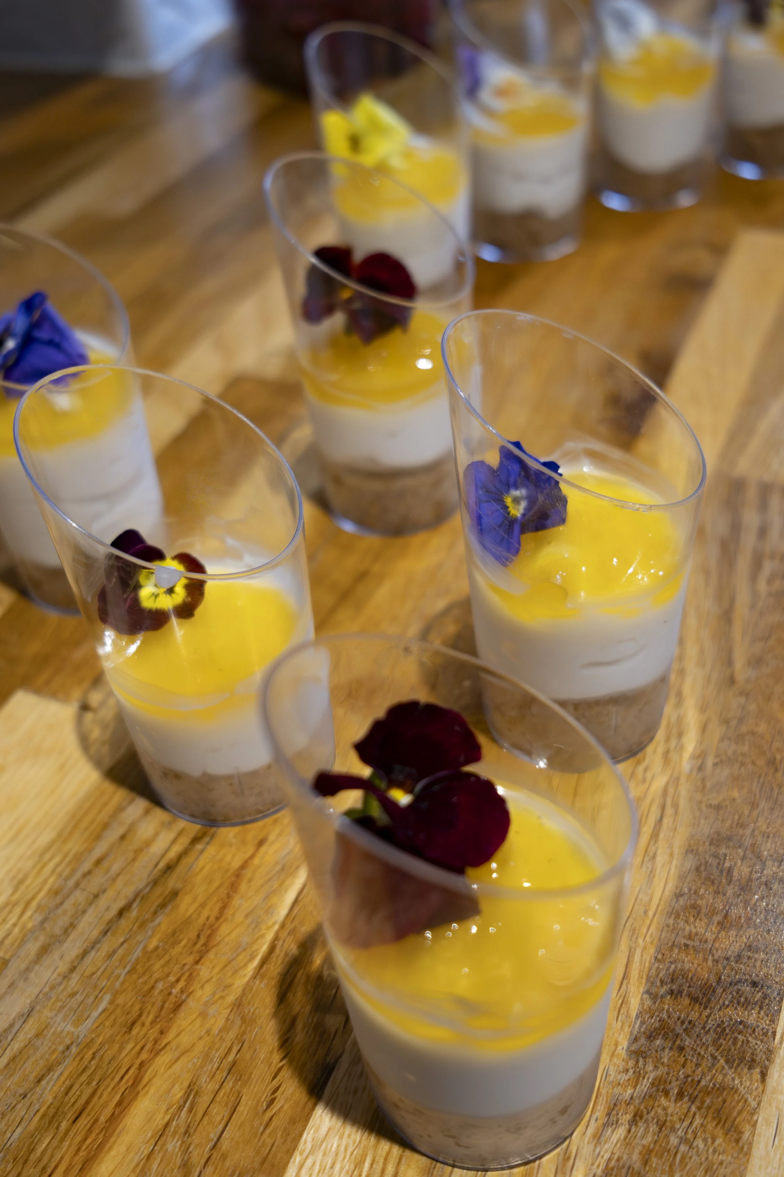 Several glasses filled with a layered dessert, topped with edible flowers and fruit, on a wooden table.