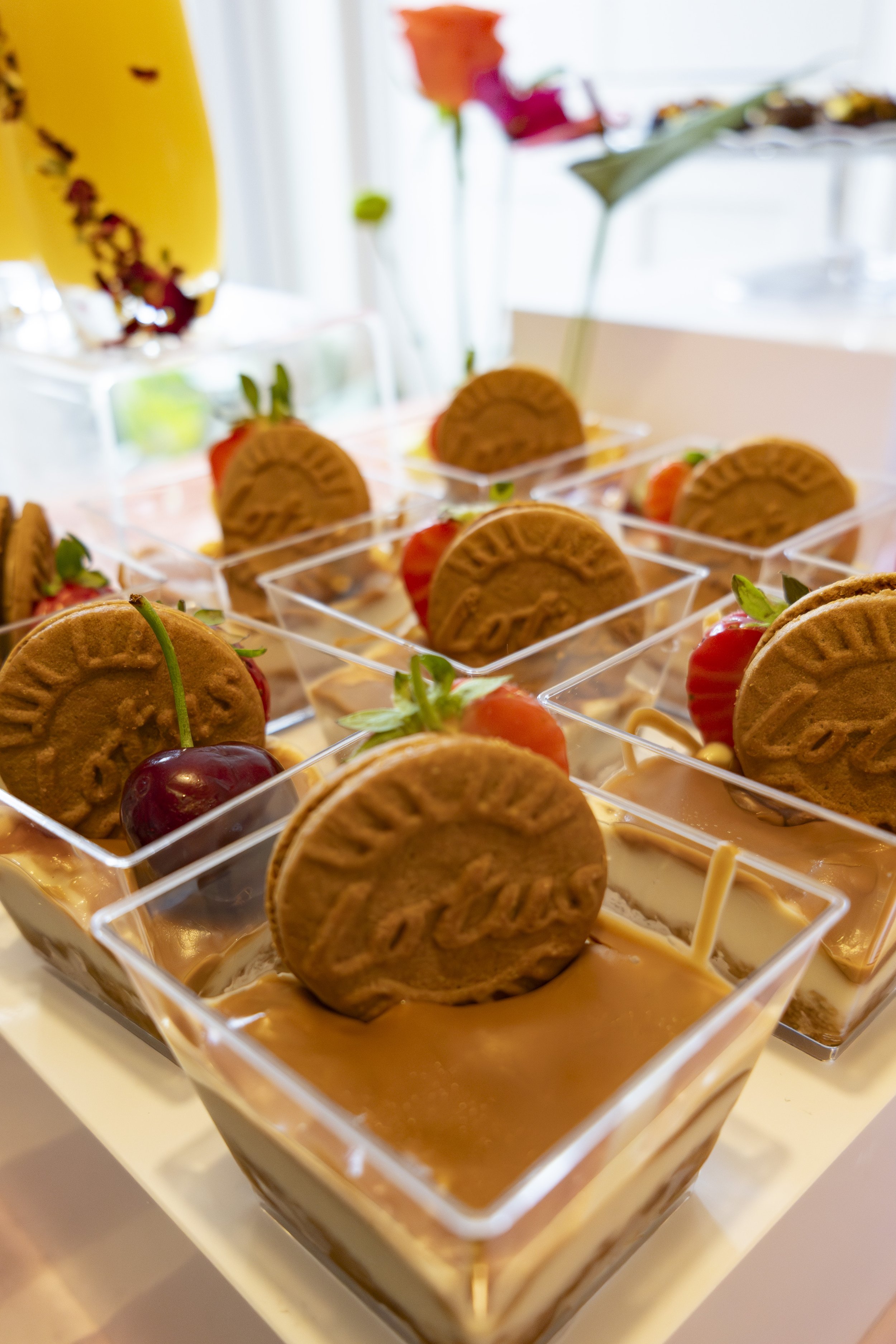 Dessert cups with caramel, topped with cookies and cherries, garnished with strawberries and mint leaves.