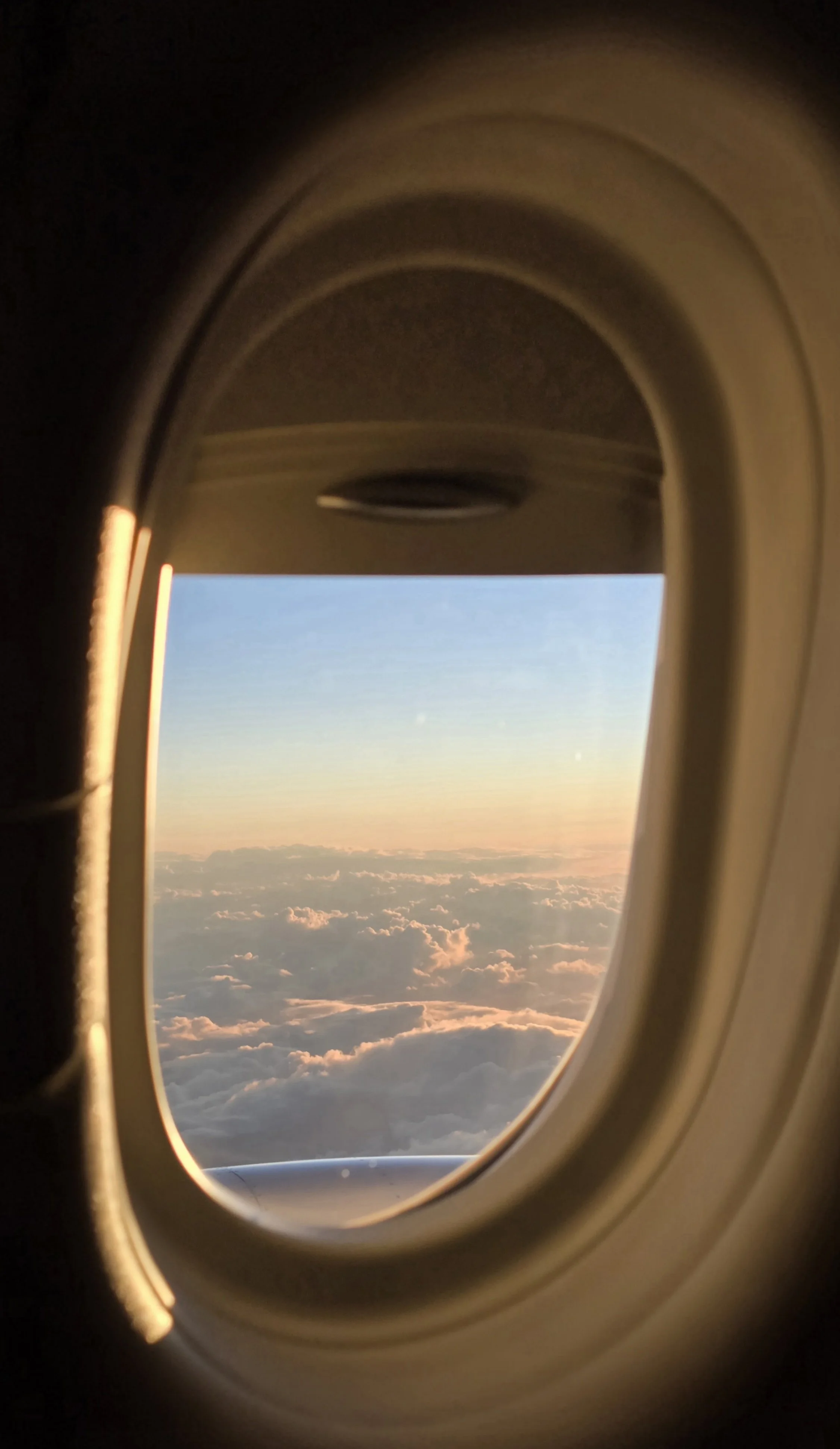 View of the sky and clouds through an airplane window during sunset.
