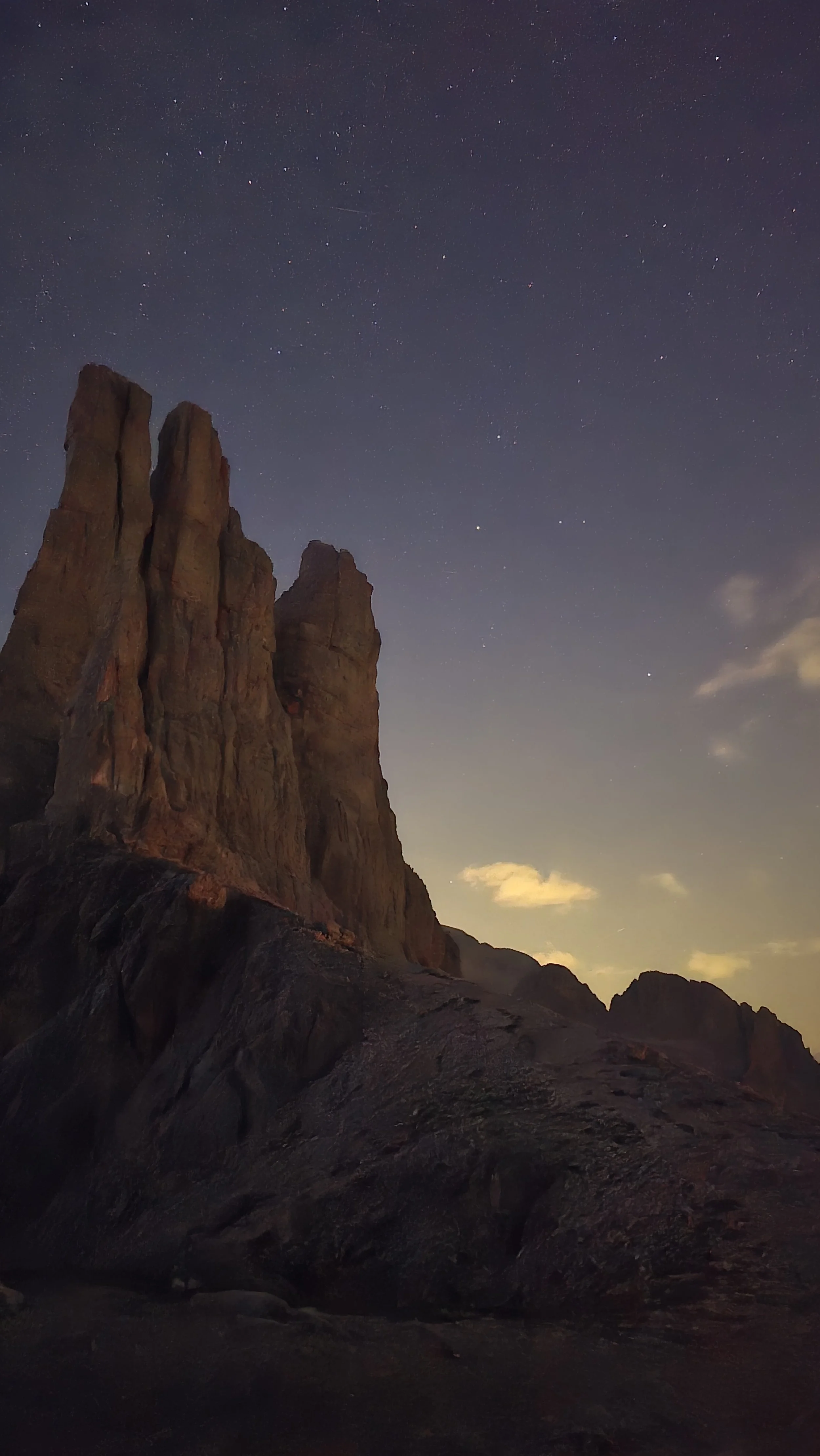 Nighttime view of tall, rugged rock formations under a star-filled sky with some clouds.