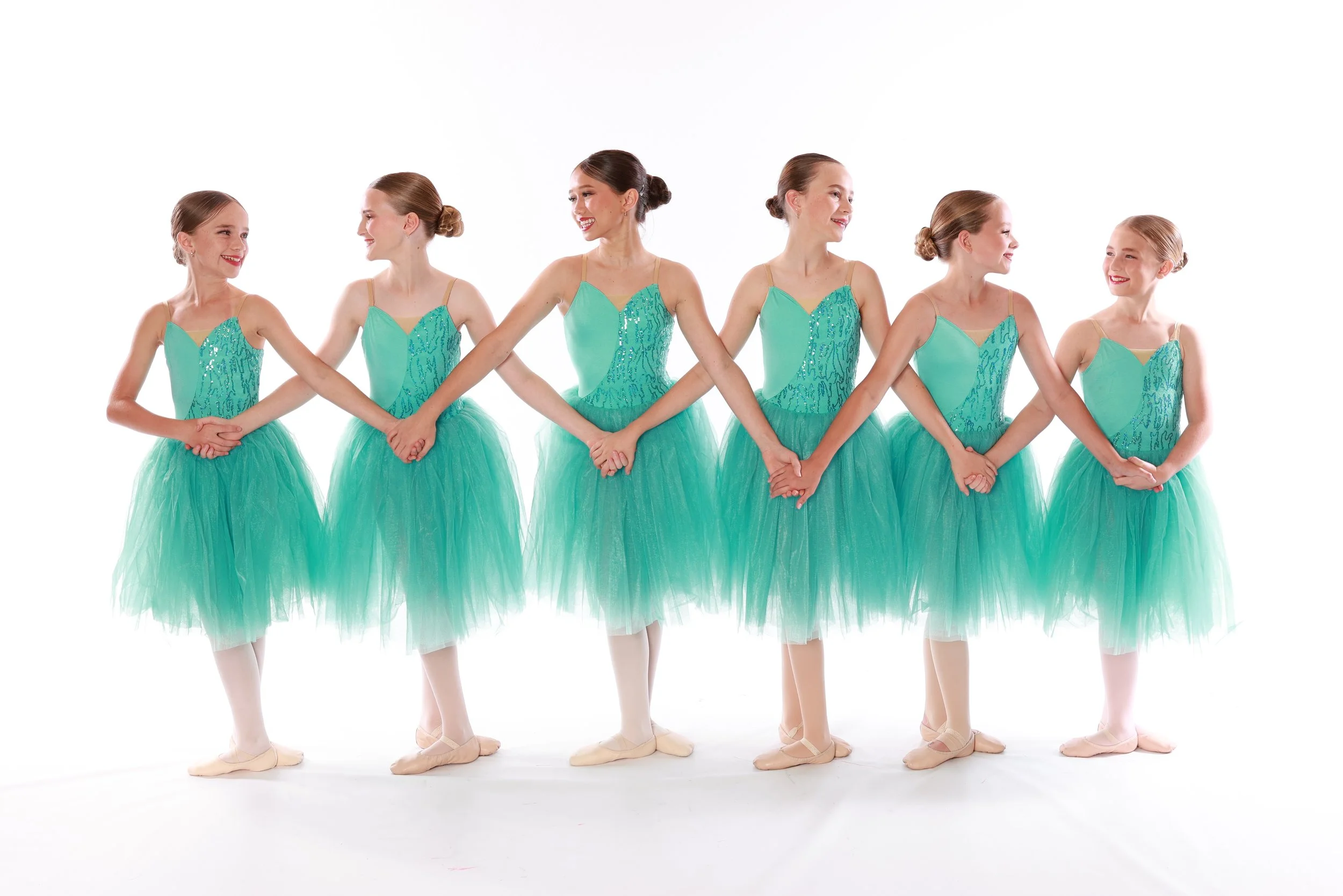 Six young ballerinas in turquoise tutus holding hands in a line