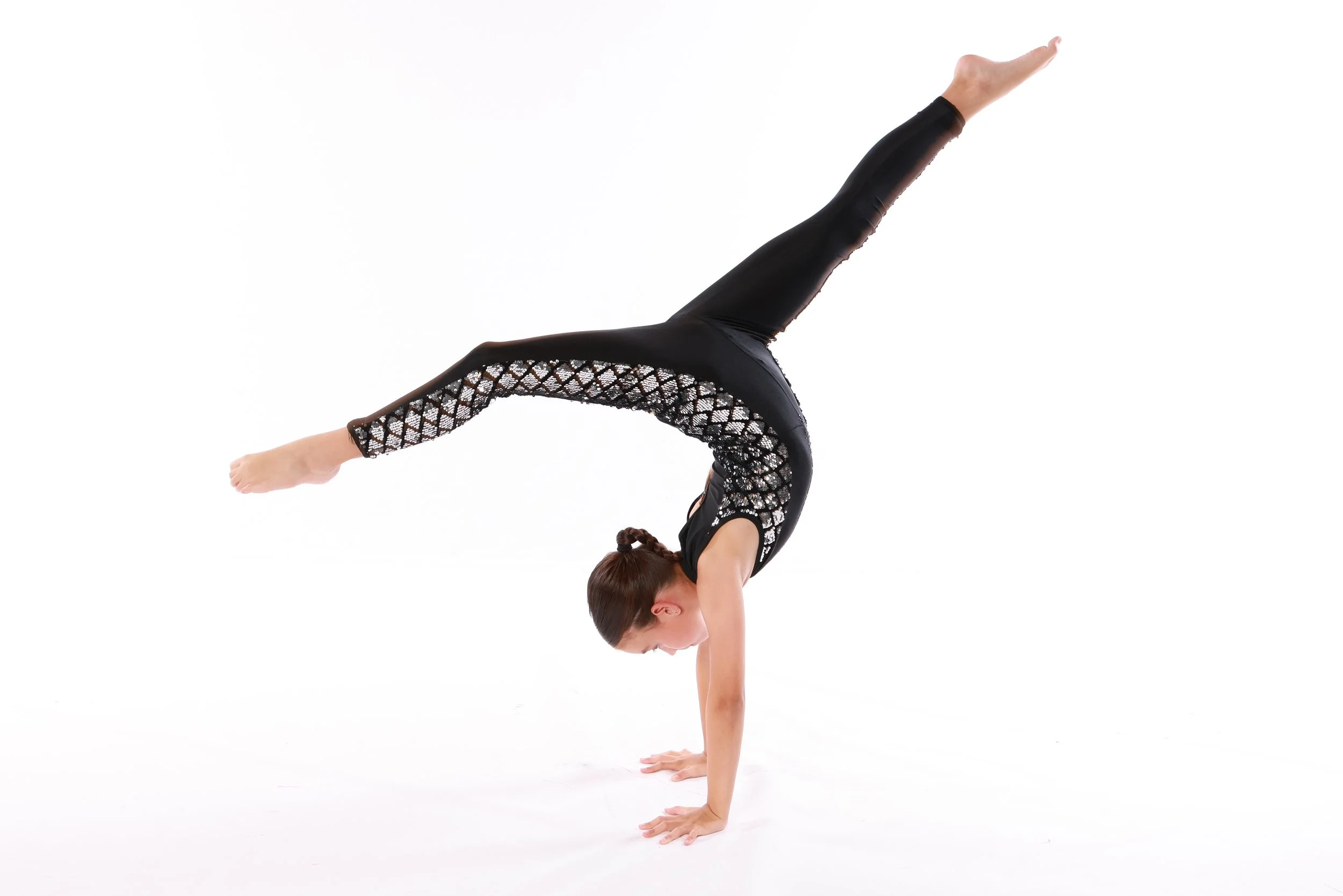 A woman performing a handstand with her legs extended upwards and one leg bent slightly at the knee, on a plain white background.