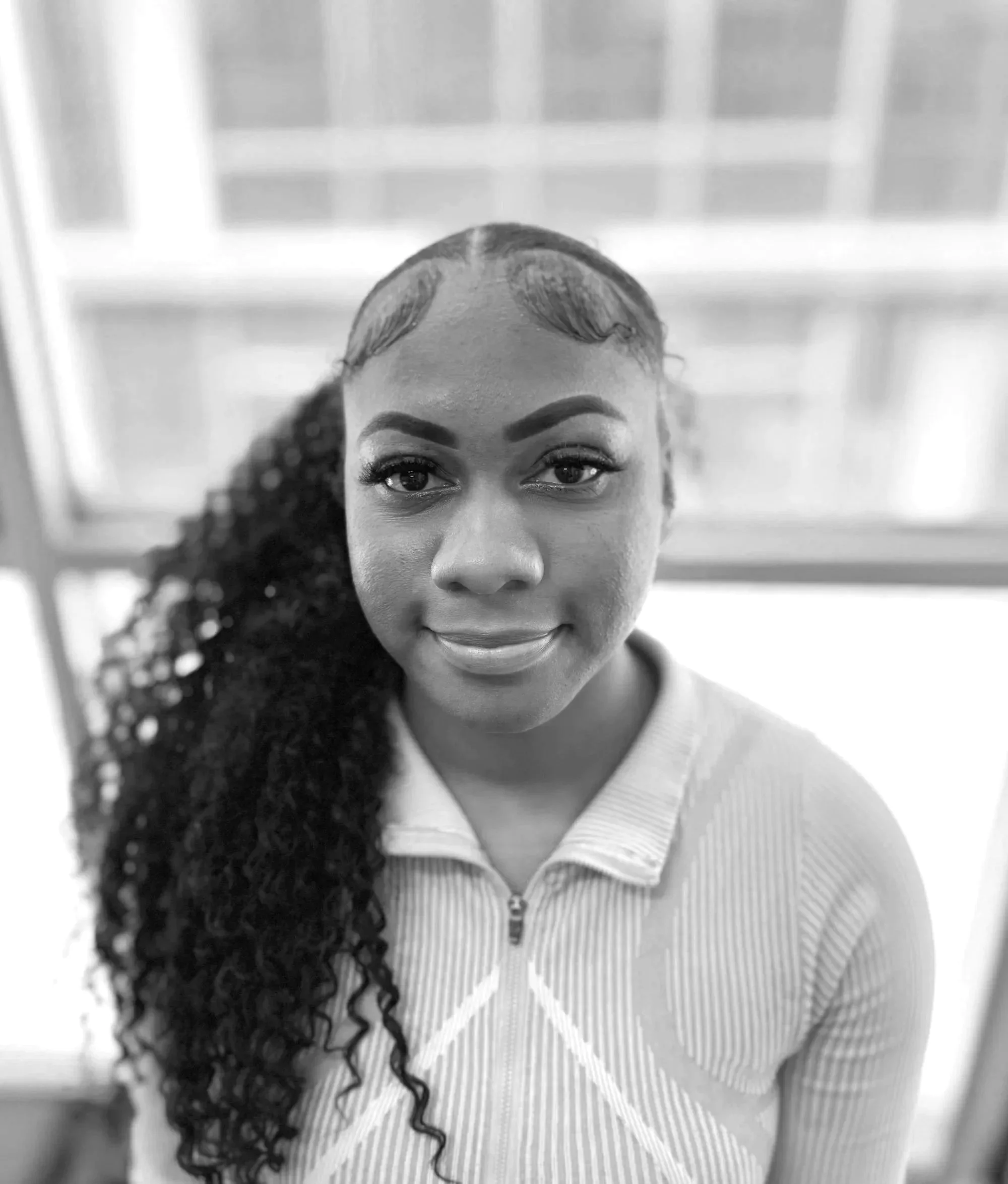 Black and white photo of a woman with braids, glasses, and a sweatshirt featuring colorful cartoon characters.