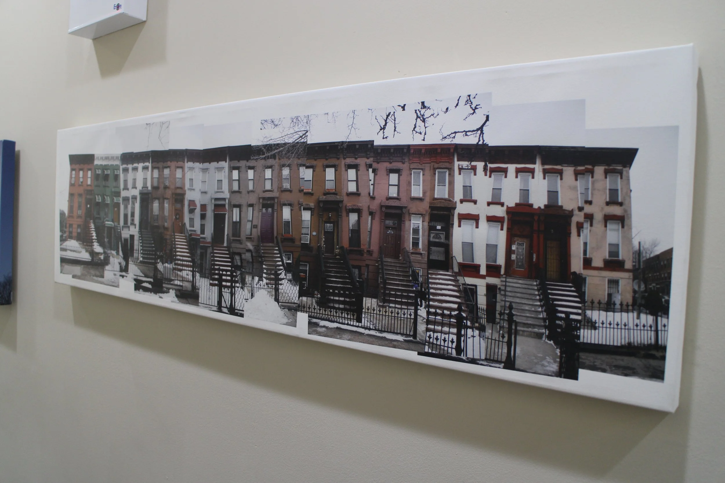 A long collage of brownstone row houses with stairs and black iron fences, snow on the ground, and leafless trees in the background.