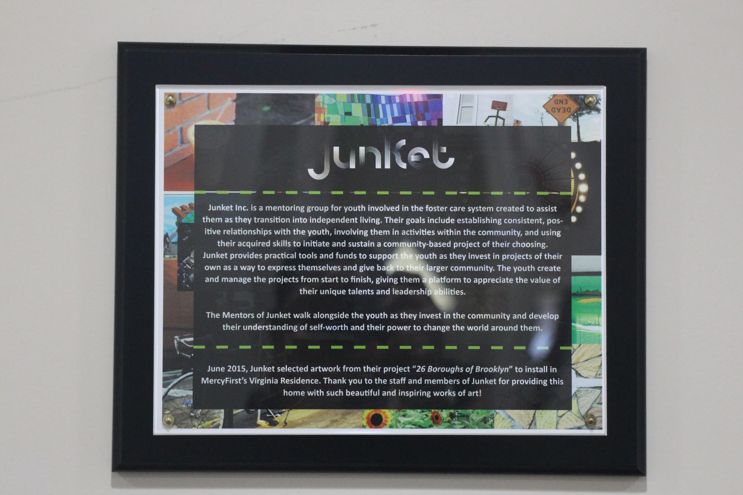 A framed informational sign about Junket Inc., a mentoring group for youth involved in foster care, with background images of artwork and community scenes.