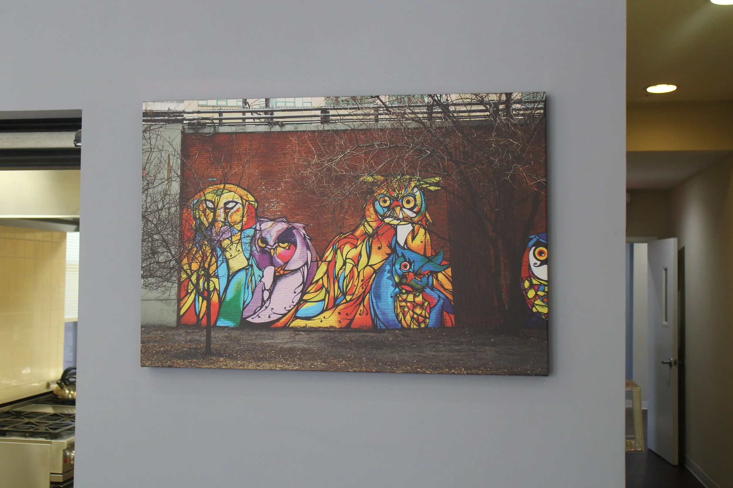 Colorful mural of various stylized animals including an owl, cat, and others painted on a brick wall, with leafless trees in the background.