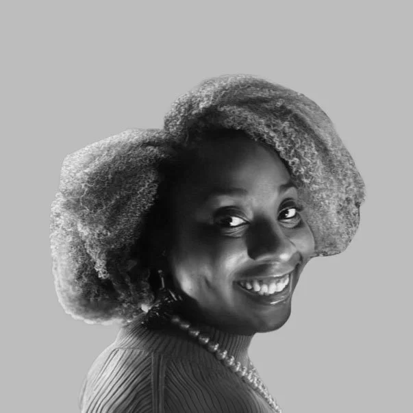A woman with a big, curly hairstyle smiling and wearing a necklace and striped top against a plain background.