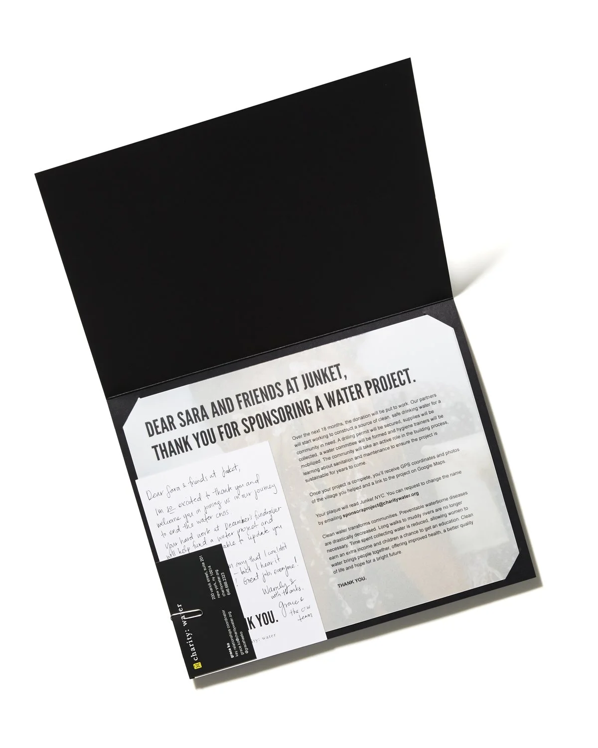 Letter of appreciation and donation confirmation from charity organization for sponsoring a water project, with a handwritten note and a black charity welcome card attached inside a black folder.
