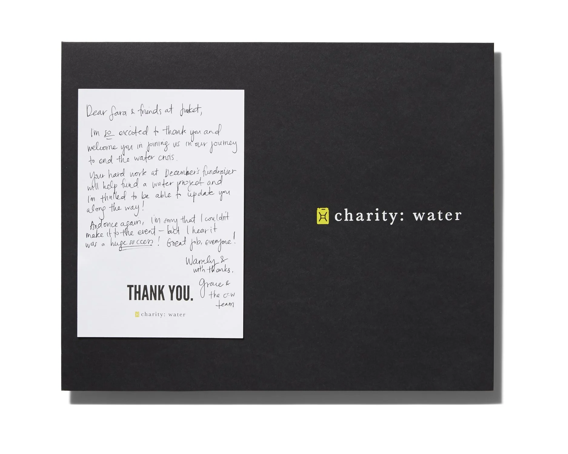 Black charity donation box with a handwritten thank you letter attached. The box has the words 'charity: water' printed on it.