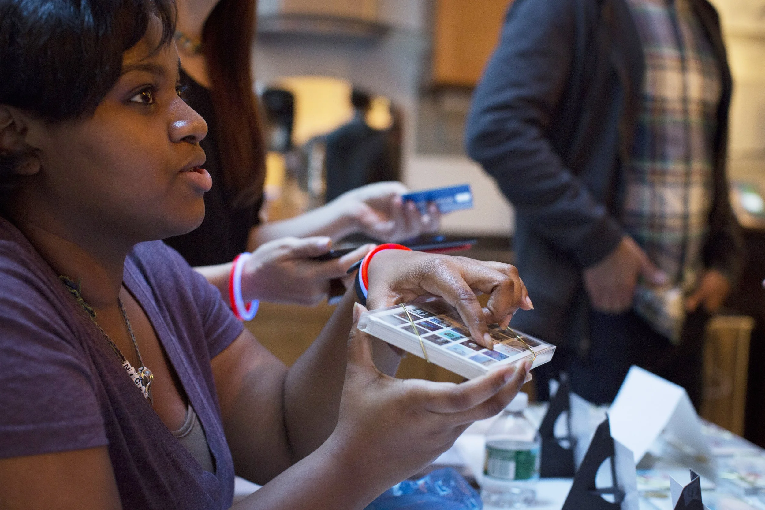 A woman looking at photo prints with other people in the background at an indoor event.