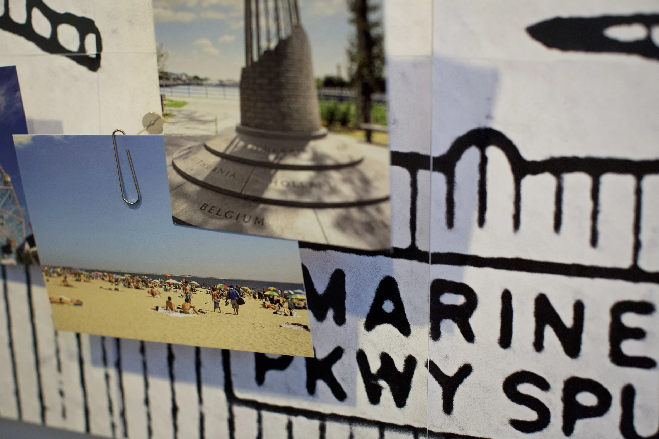 Collection of photographs attached to a board, including a picture of a sandy beach with people, a photo of a monument with the word 'Belgium,' and an image of black graffiti on white wall.