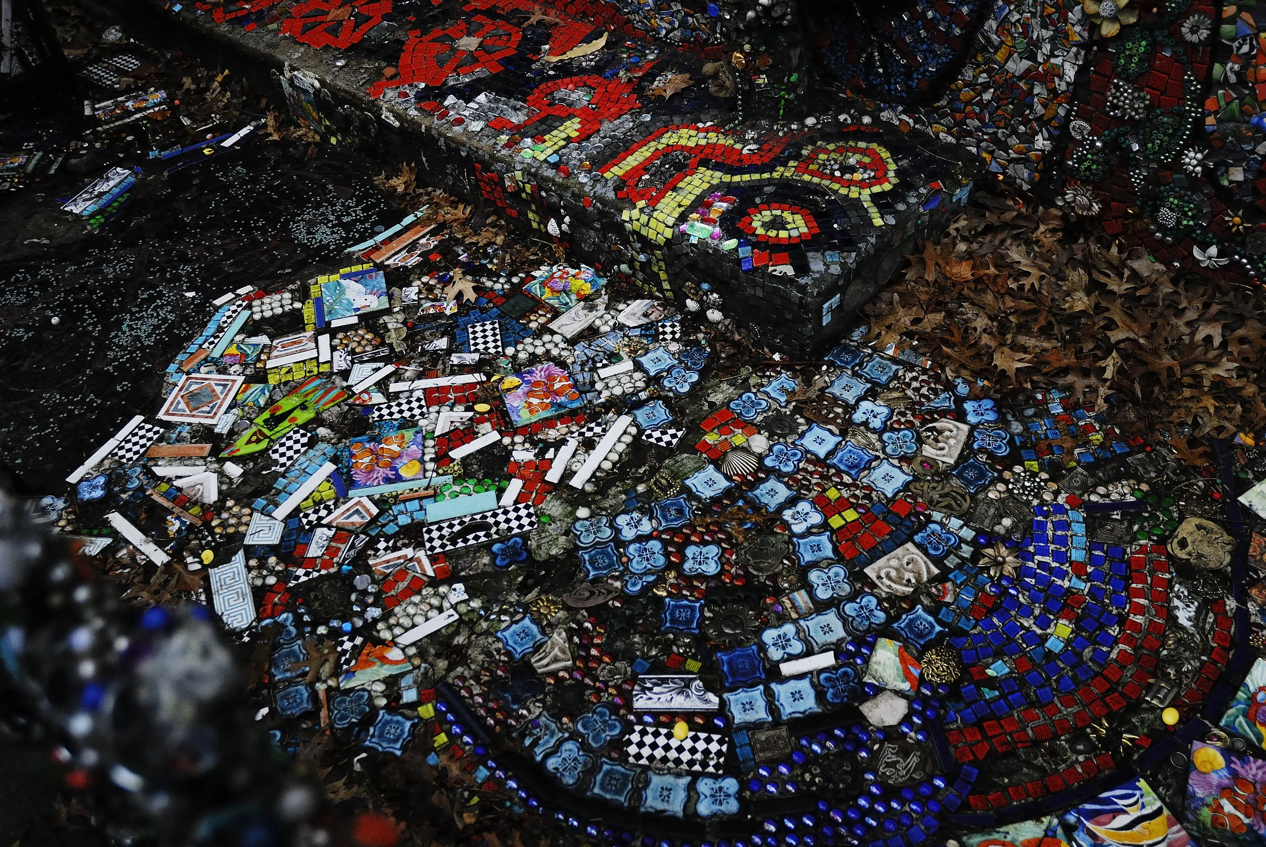 Colorful mosaic composed of various small tiles, beads, and other decorative objects arranged on a surface.
