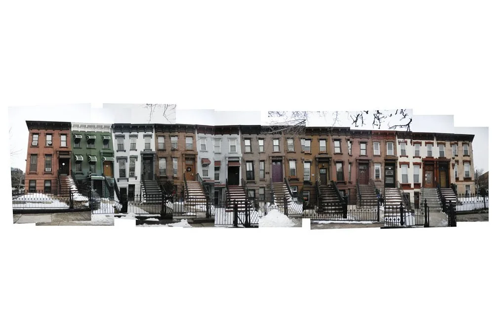 Row of colorful row houses with snow on the ground, stairs leading up to each entrance, and black fences in front.