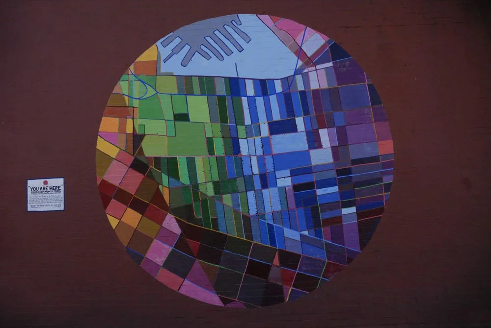 Colorful circular mural depicting an abstract map with various colored sections and lines on a red brick wall.