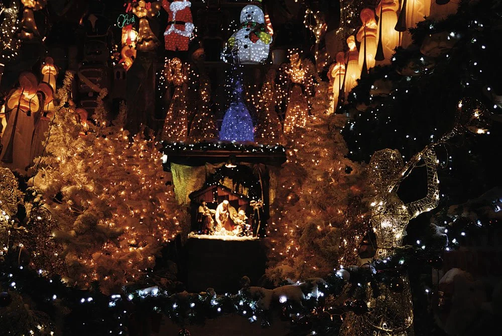Christmas display with illuminated trees, nativity scene, snowman figure, and various holiday decorations in warm lighting.