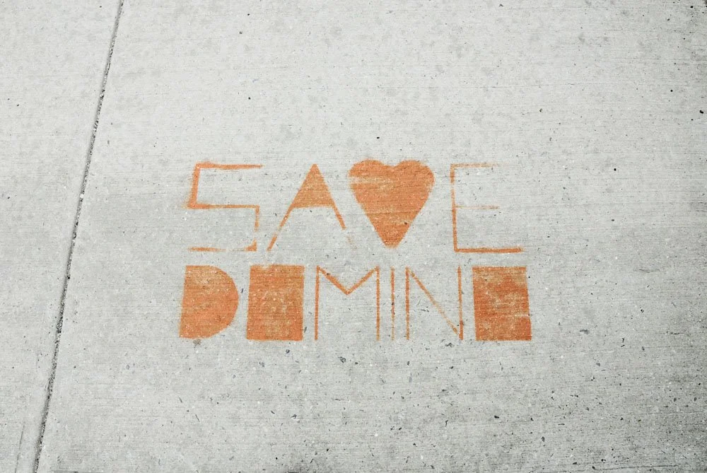 Concrete sidewalk with orange chalk writing that says "Save the Dime" with the letter "O" replaced by a heart shape.