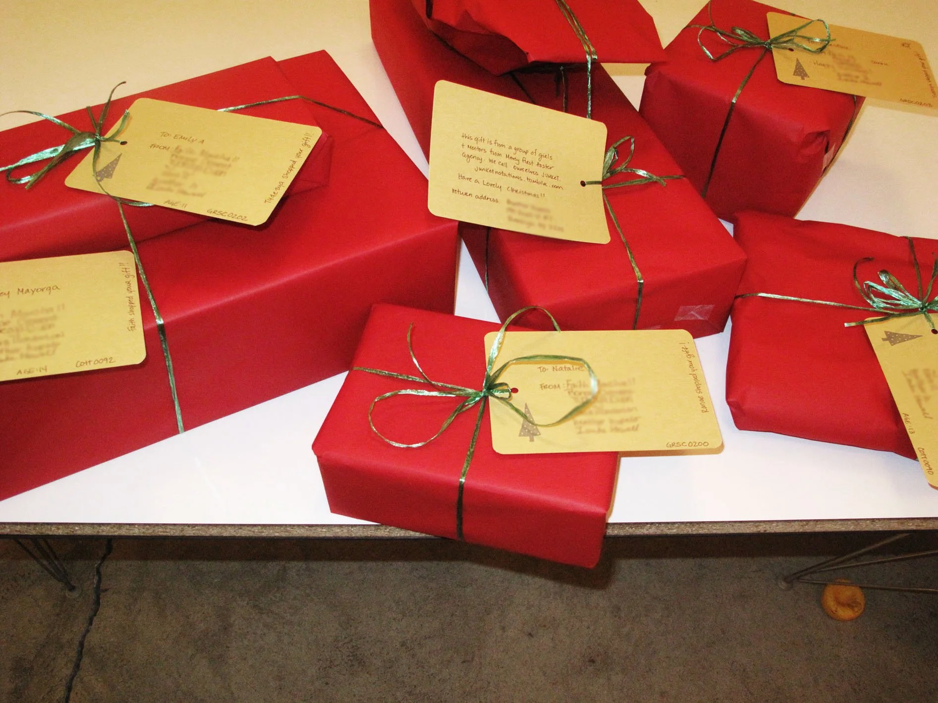 Several wrapped Christmas gifts in red paper with yellow tags and green ribbon bows on a white surface.