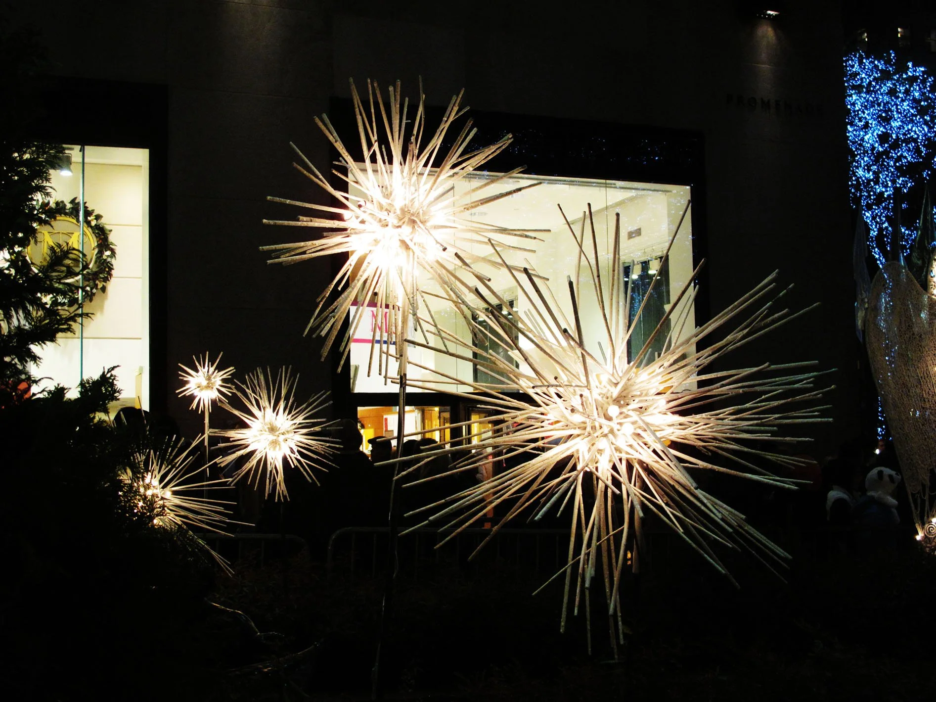 Outdoor display of illuminated star-shaped holiday decorations at night in front of a dark building with windows and Christmas lights.