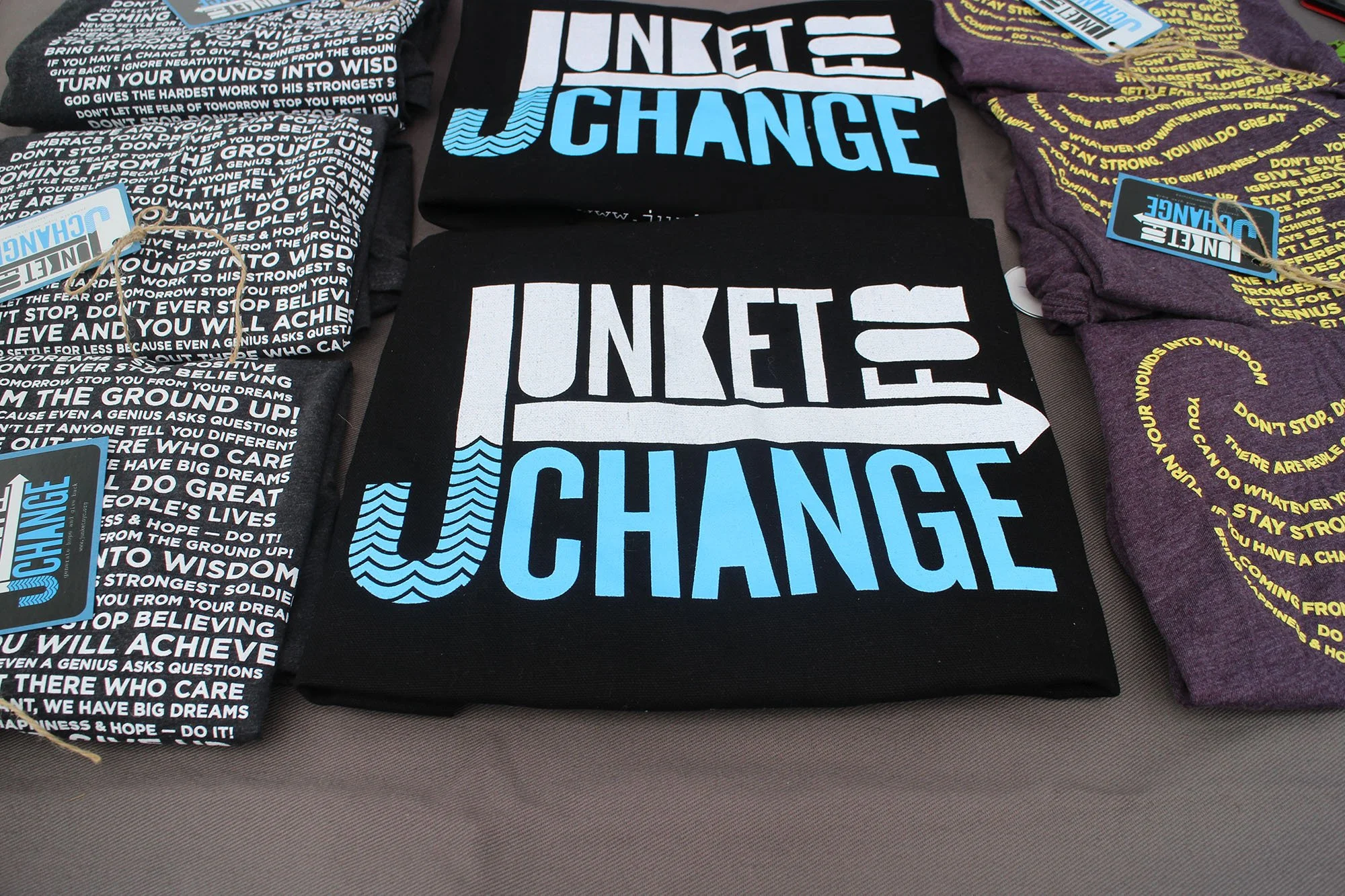 T-shirts with motivational text and designs, featuring the phrase 'JUNKETS OF CHANGE' in large white and blue lettering on the black shirt in the center.