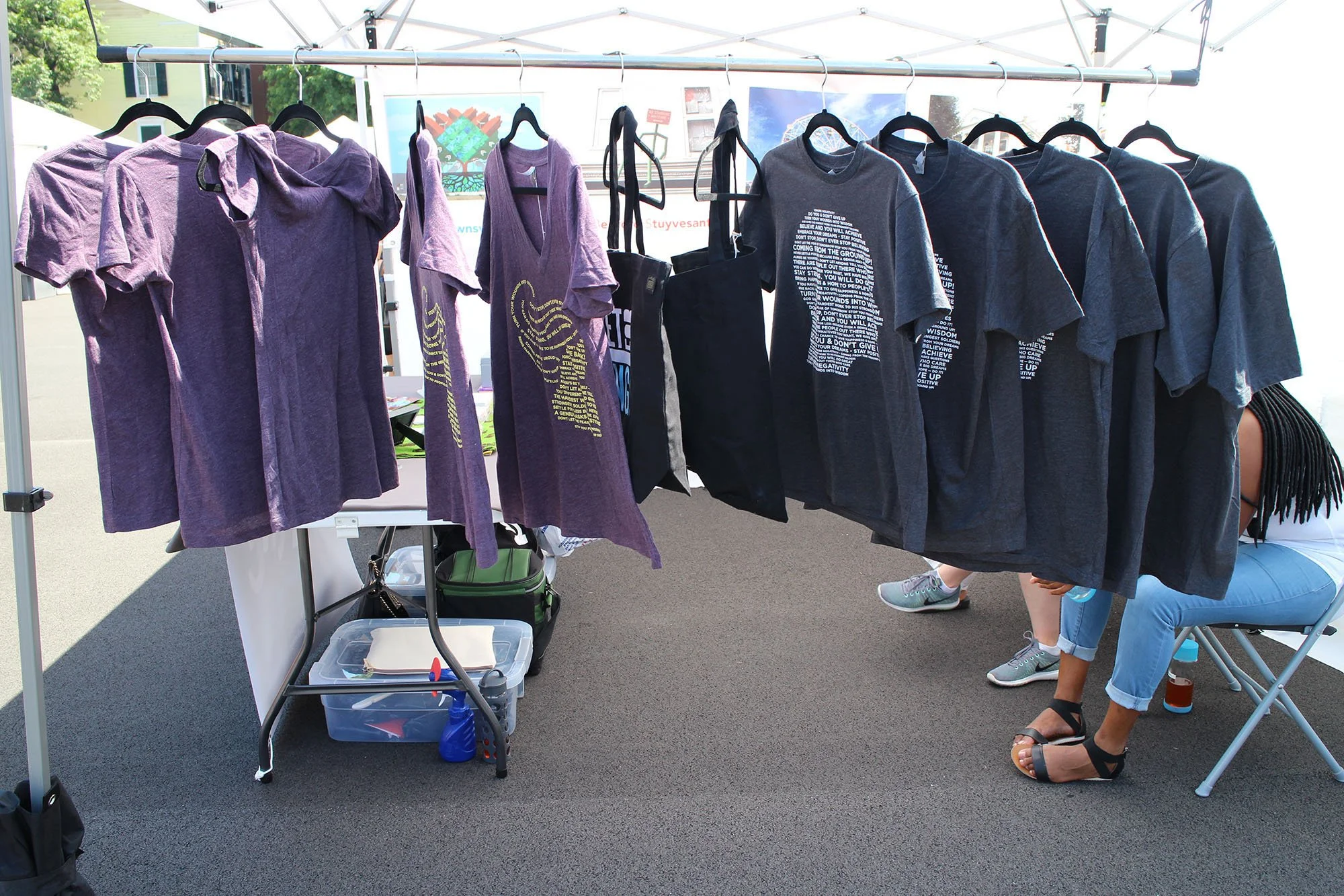 A display of purple and black T-shirts and hoodies hanging on a rack at an outdoor market
