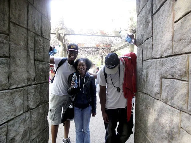 Three people standing in a stone archway at an amusement park, smiling and posing for a photo. Two men and one woman, with the woman holding a water bottle.