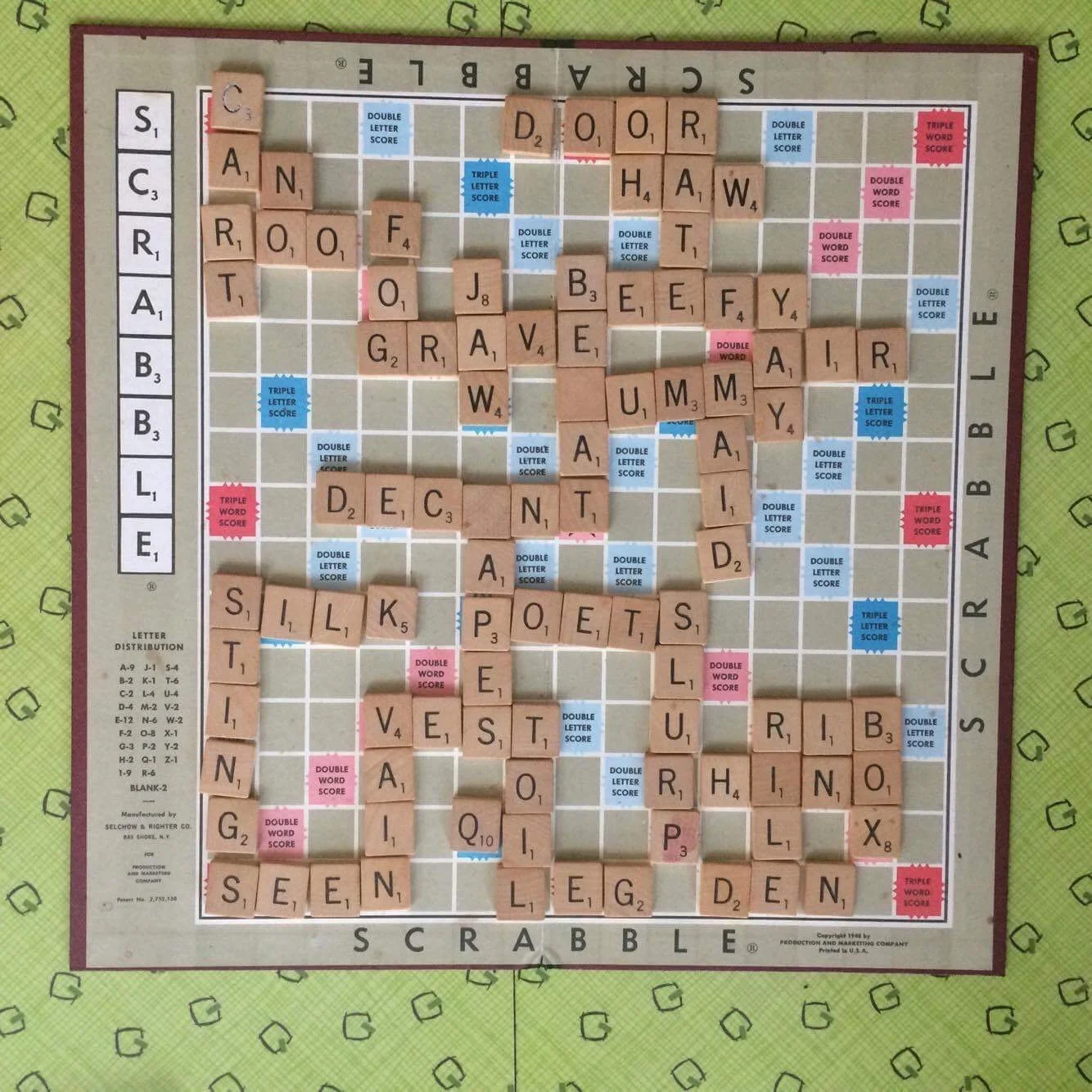 A Scrabble game board with words like 'CAN', 'FOG', 'DOOR', 'HAT', 'SILK', 'POET', 'VENT', and 'DEAR' spelled out using letter tiles, along with score markers and bonus spaces visible.