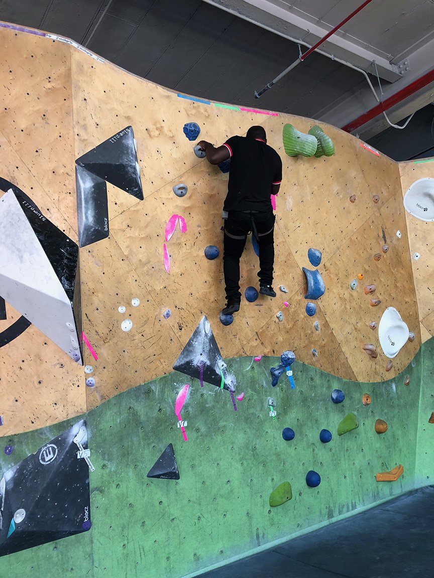 A person climbing an indoor bouldering wall with various colored holds.