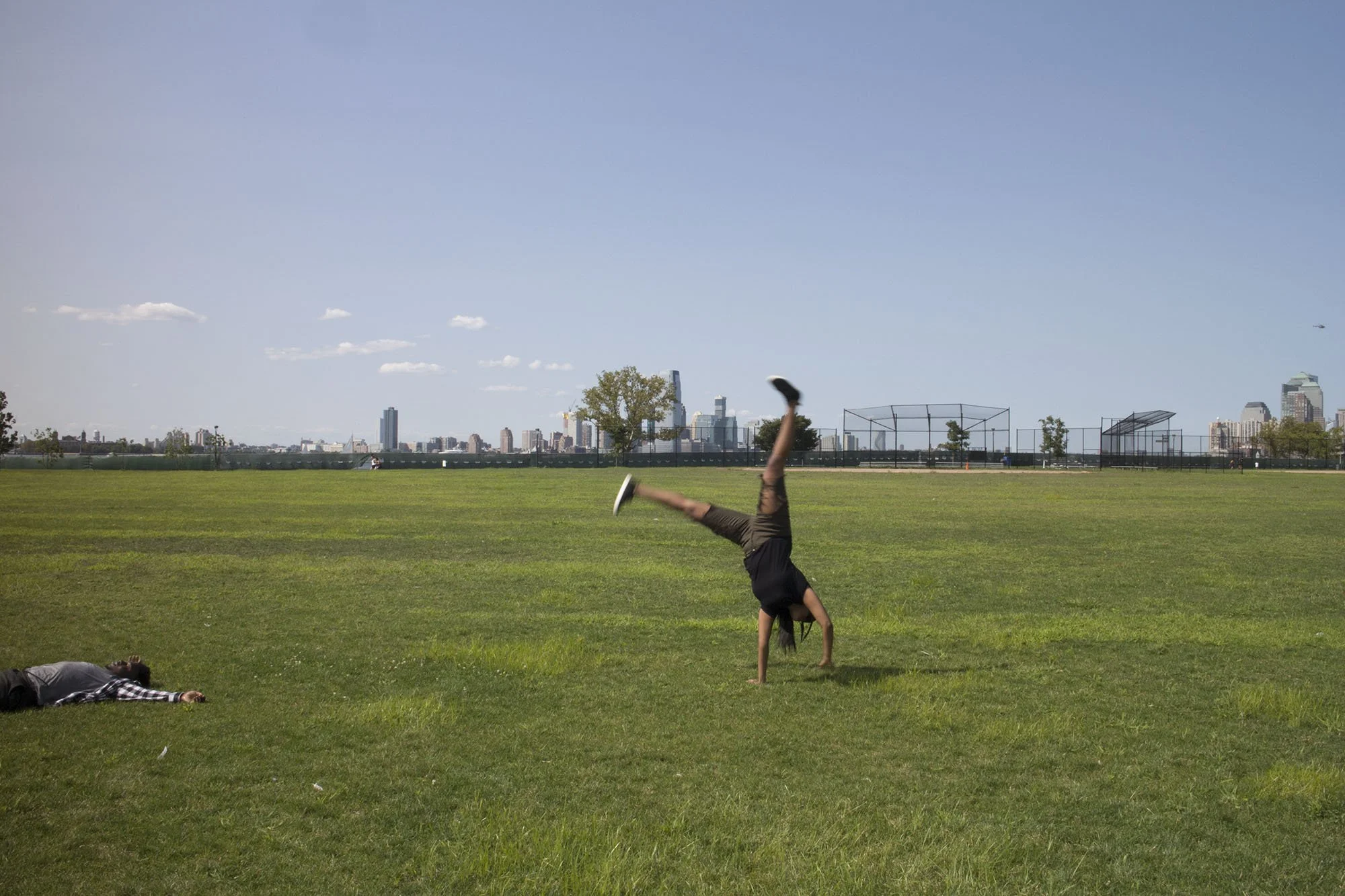 Person performing a handstand on a grassy field in a park with a city skyline in the background.