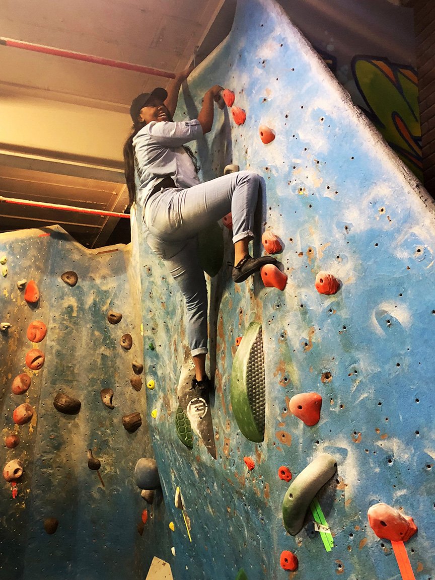 A woman climbing an indoor rock wall with colorful holds.