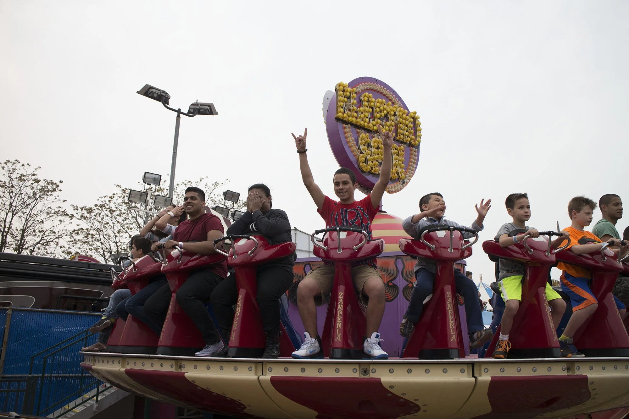 People riding the zipper amusement ride at an amusement park with a large purple and yellow sign reading 'Zipper' in the background.