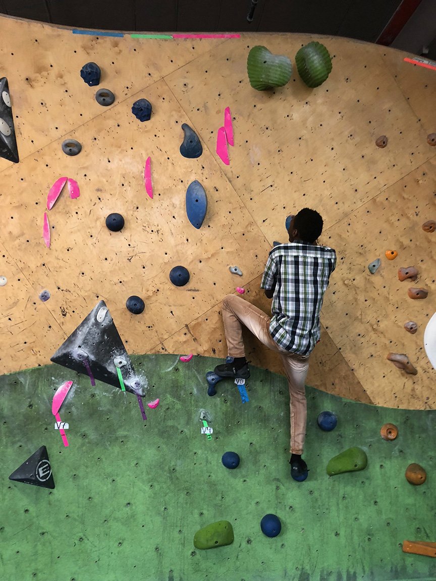 A person climbing an indoor bouldering wall with various colorful holds and grips.