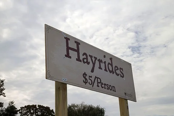 A sign advertising hayrides for five dollars per person, with a cloudy sky in the background.