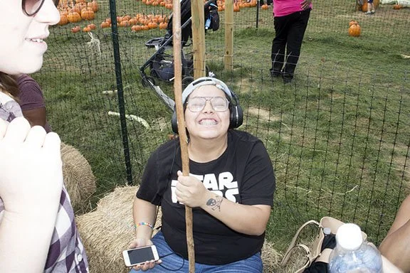 Woman smiling with eyes closed, wearing headphones and holding a stick, at pumpkin patch.