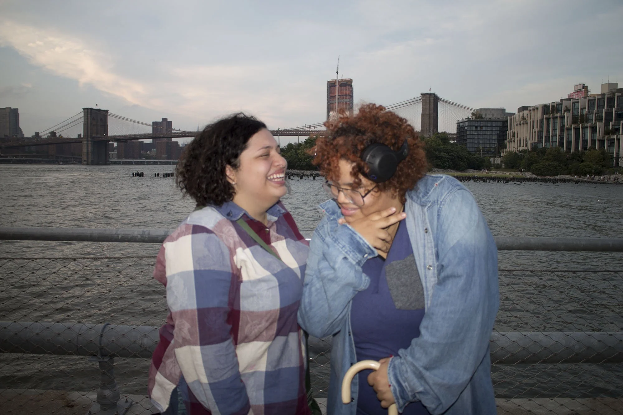 Two women laughing and having fun by the waterfront with city skyline and bridge in the background.