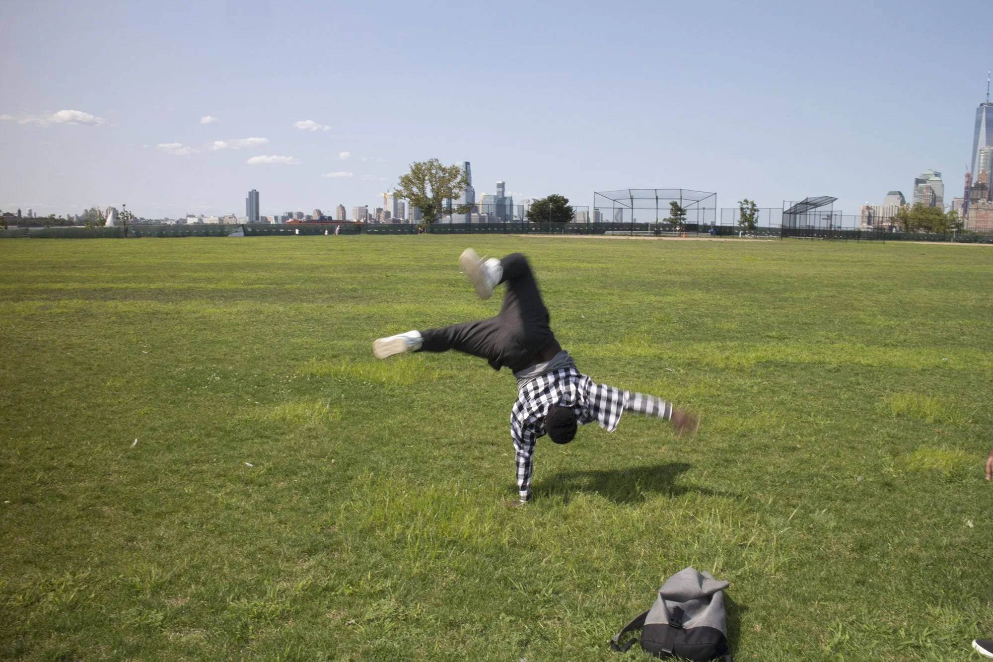 Person performing a cartwheel on a grassy field with a city skyline in the background.